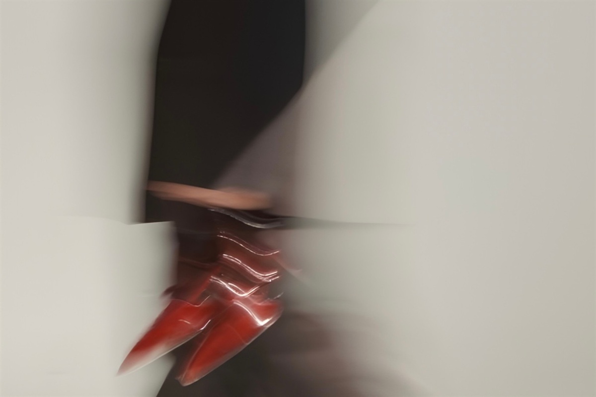Motion-blurred shot of a person in red heeled boots and a dark skirt walking past a pale wall