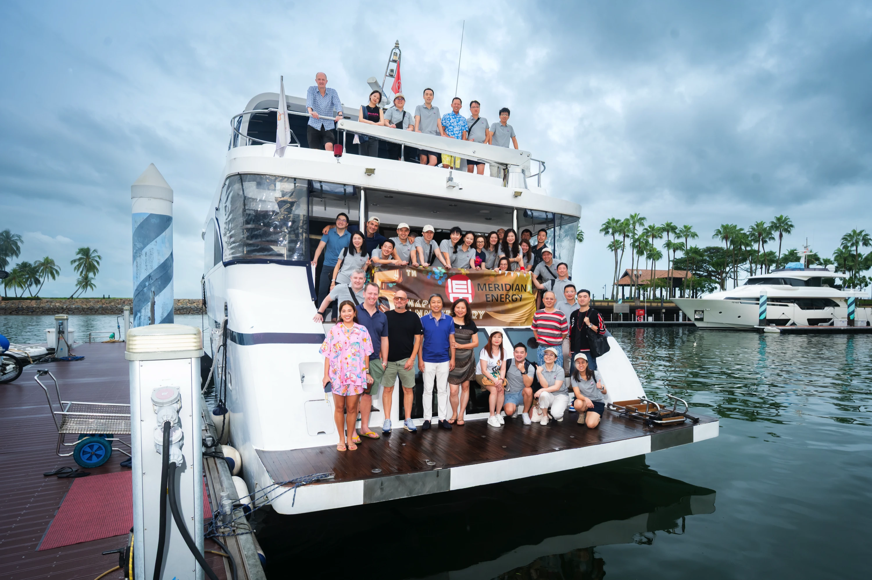 Group of people posing on a docked white yacht, holding a banner that reads Meridian Energy.