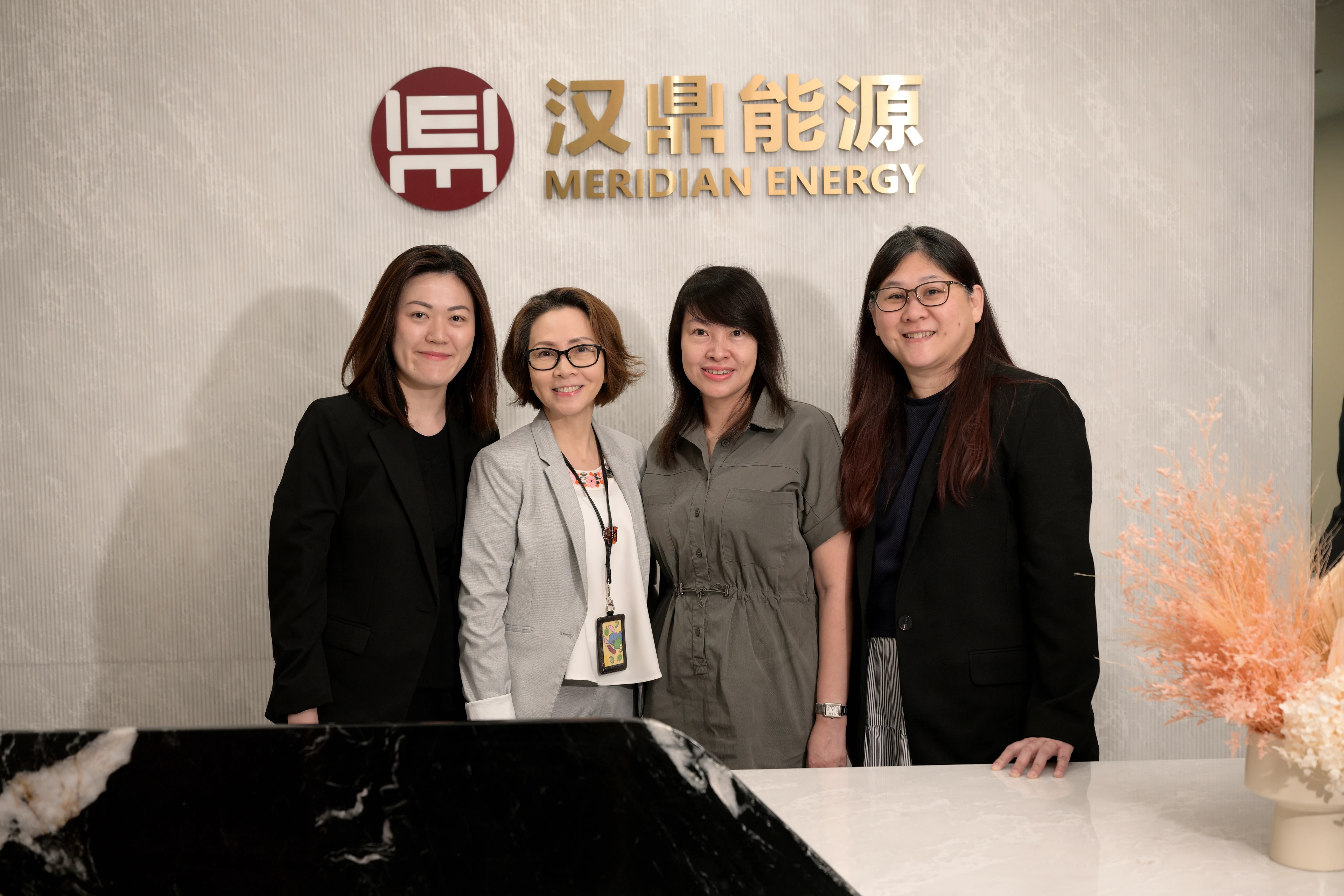 Four women stand smiling in front of a wall with Meridian Energy logo and text.