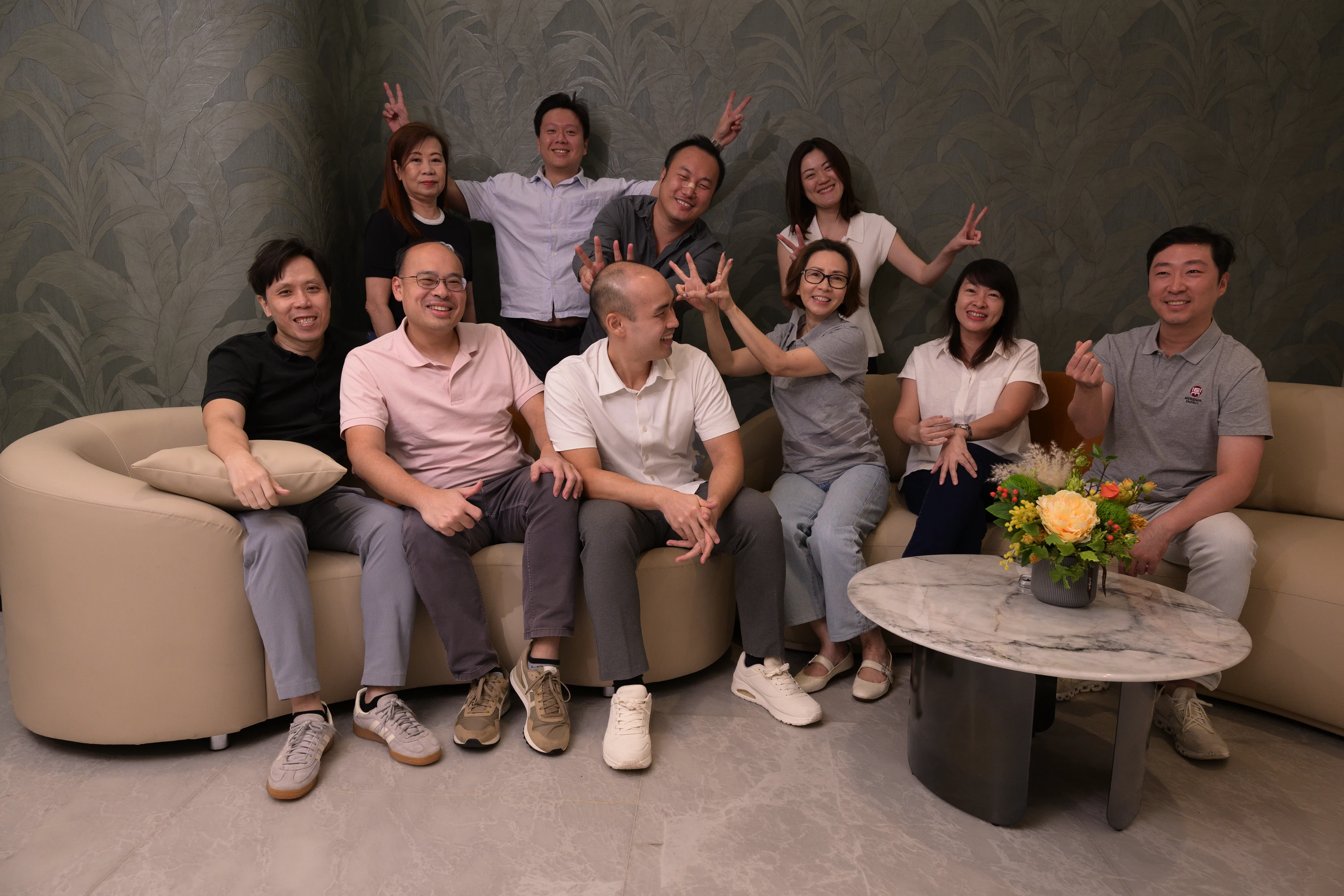 Group of ten adults sitting and standing in a living room with smiles and playful gestures.