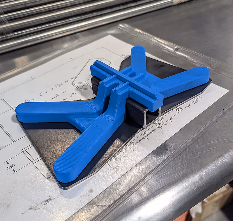 3D-printed process fixture positioned over a fabricated metal component and engineering drawing.