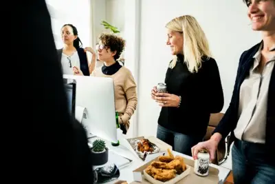 Four casually dressed people chatting near a desk with snacks and drinks in a bright office.