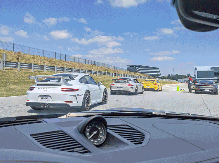 Four sports cars lined up on a race track with a blue sky and grassy embankment on the side.