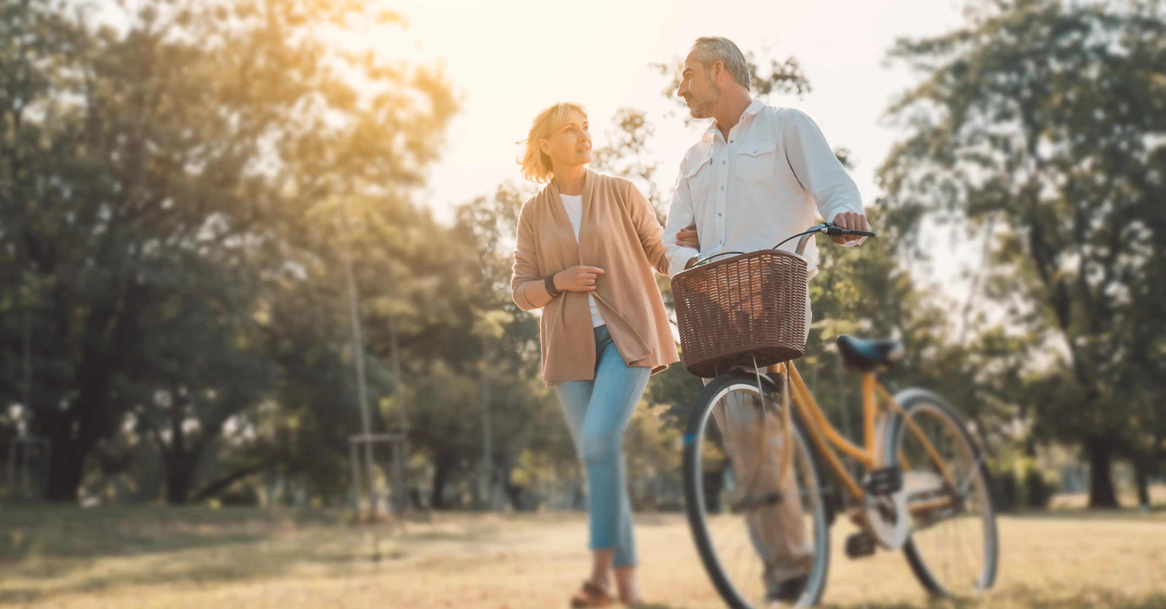 Couple walking with a bicycle together in a sunlit park