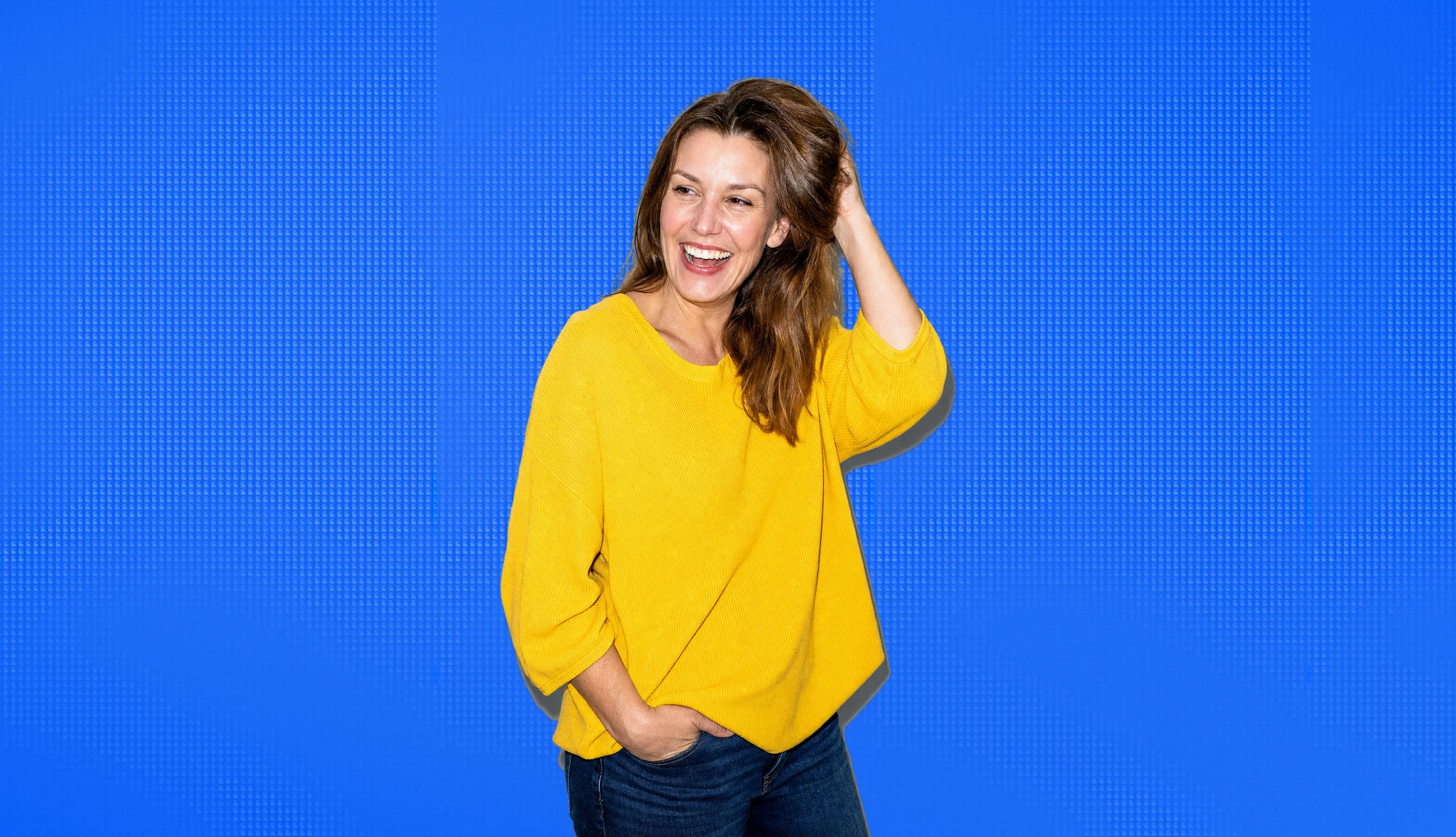 A woman in her forties laughing, hand in her hair