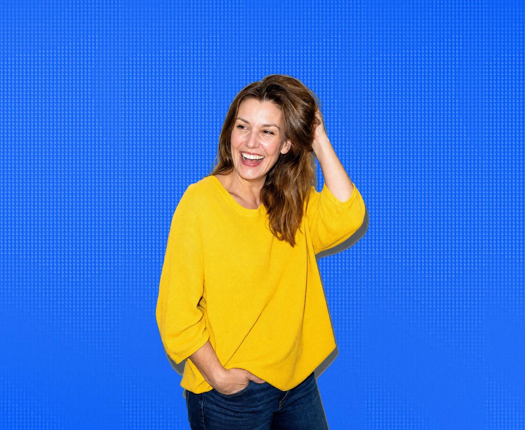 A woman in her forties laughing, hand in her hair