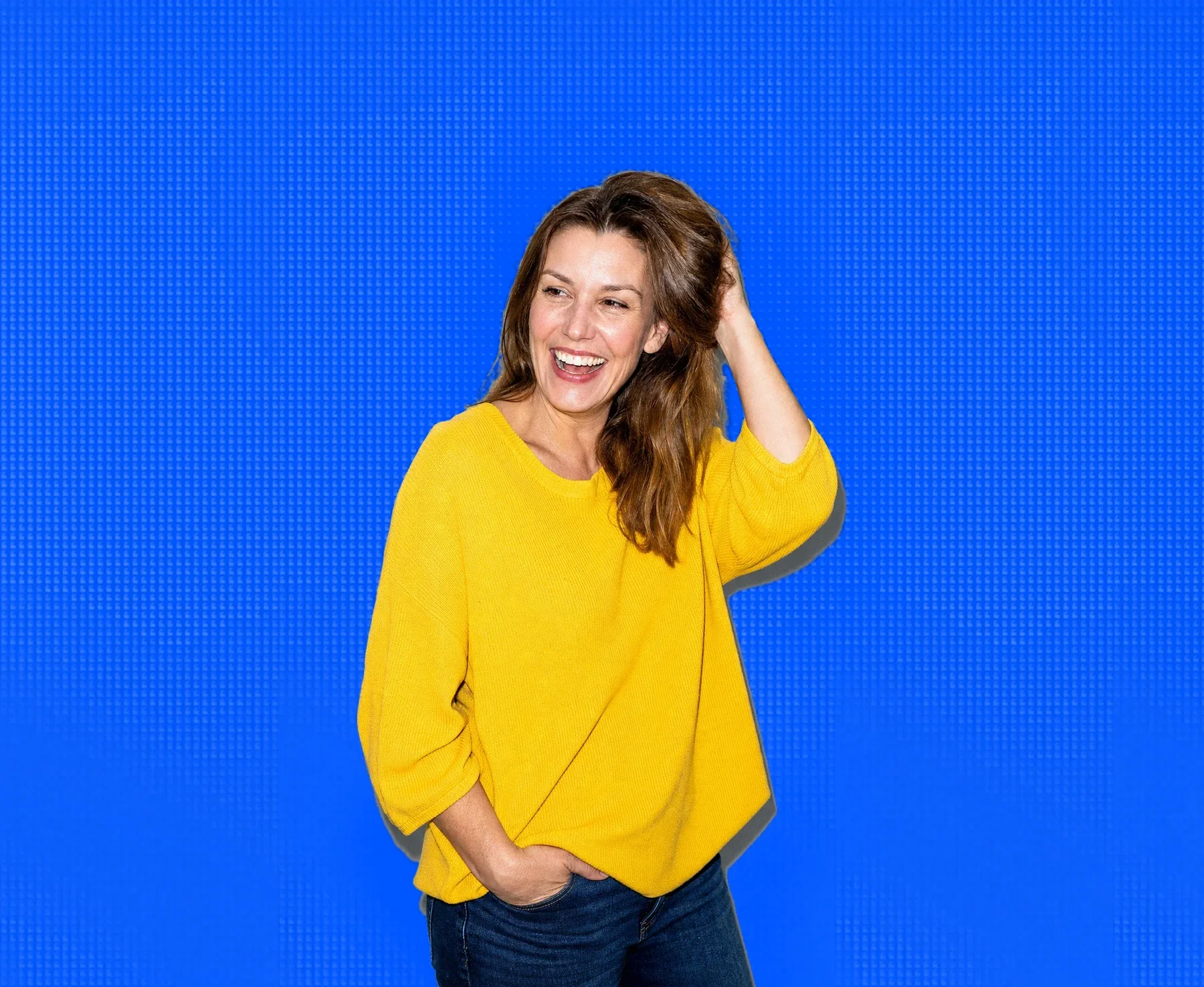 A woman in her forties laughing, hand in her hair