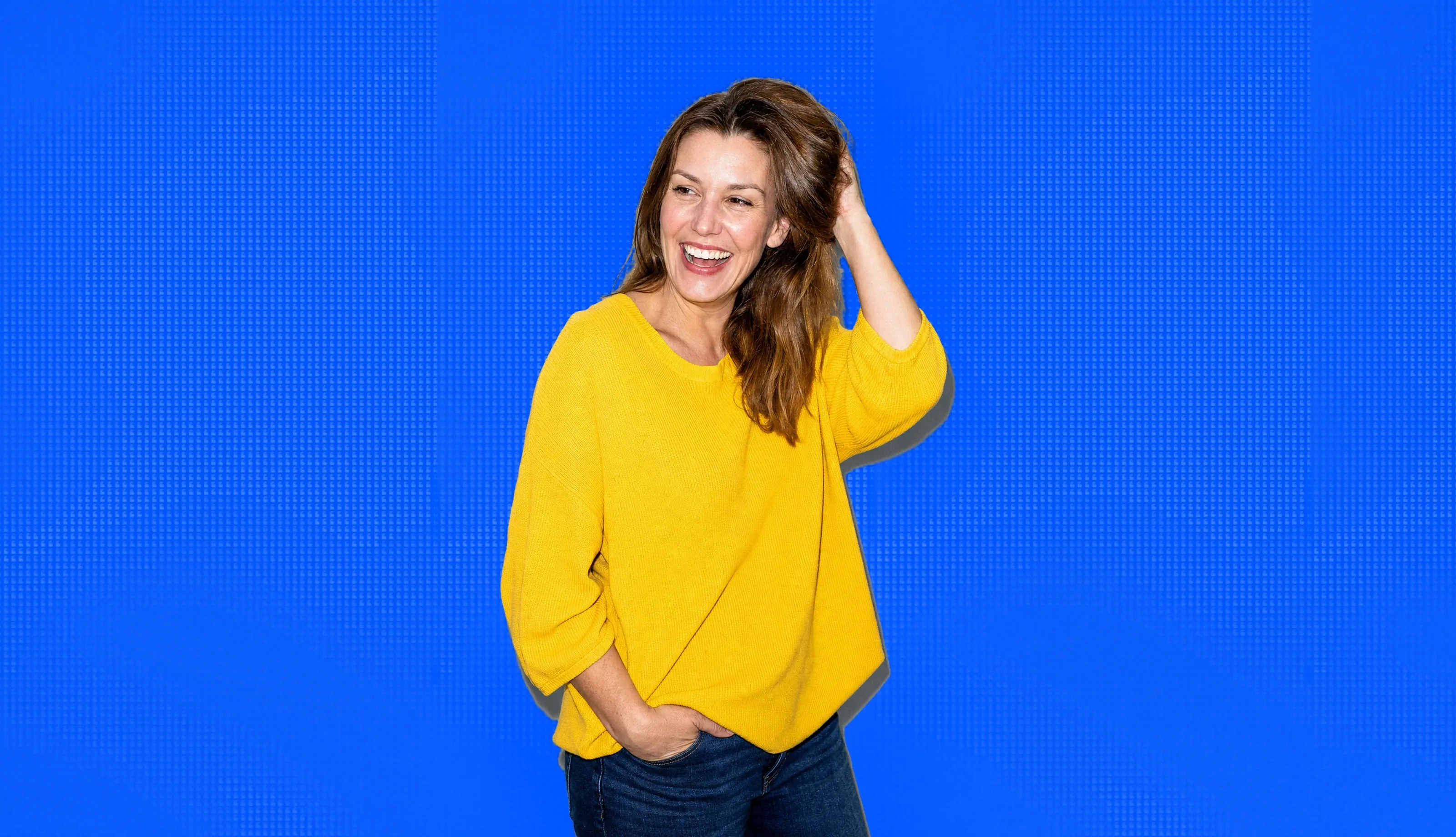 A woman in her forties laughing, hand in her hair