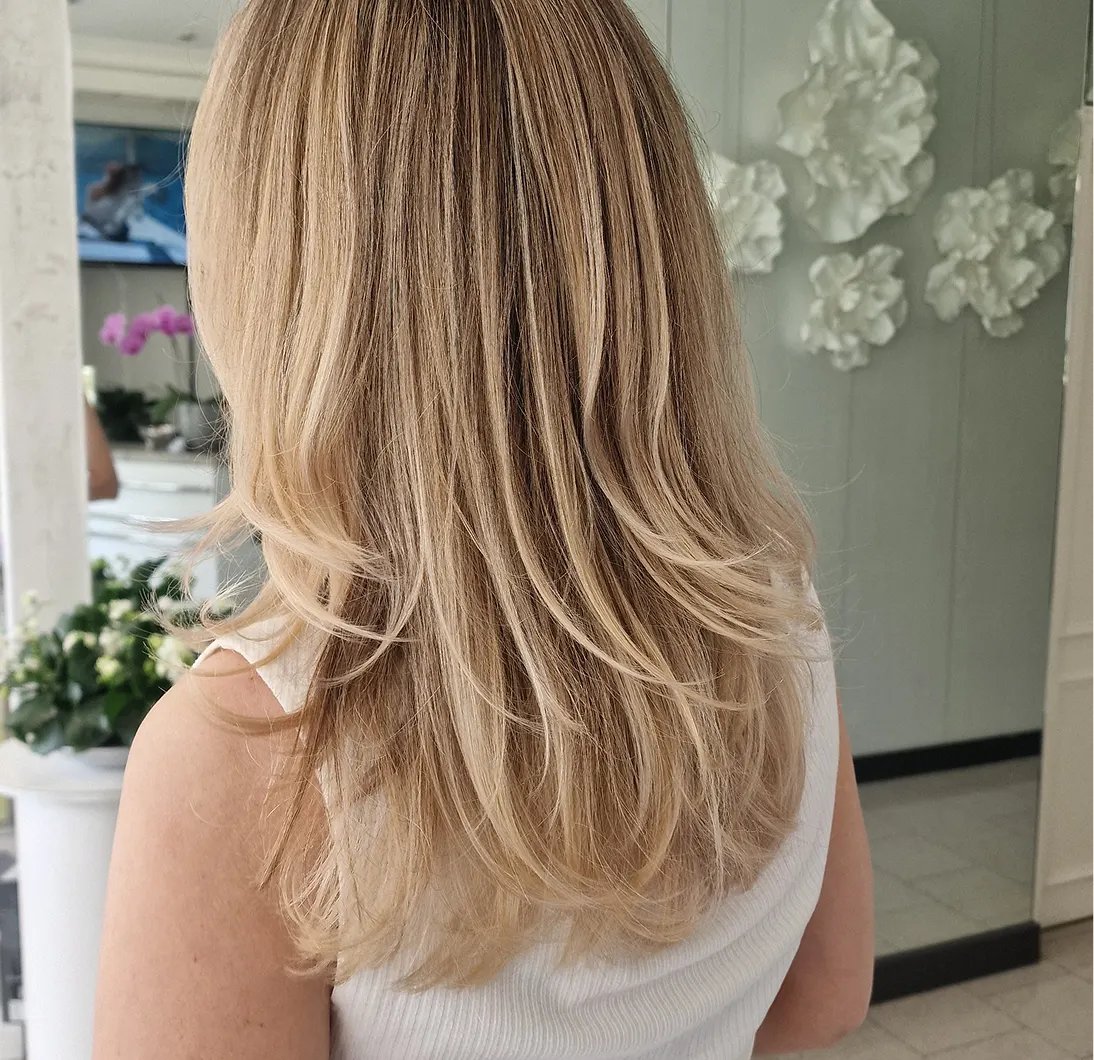 Kundin im Friseursalon mit Foliensträhnen im Haar, während die Stylistin ein Spiegel-Selfie macht.