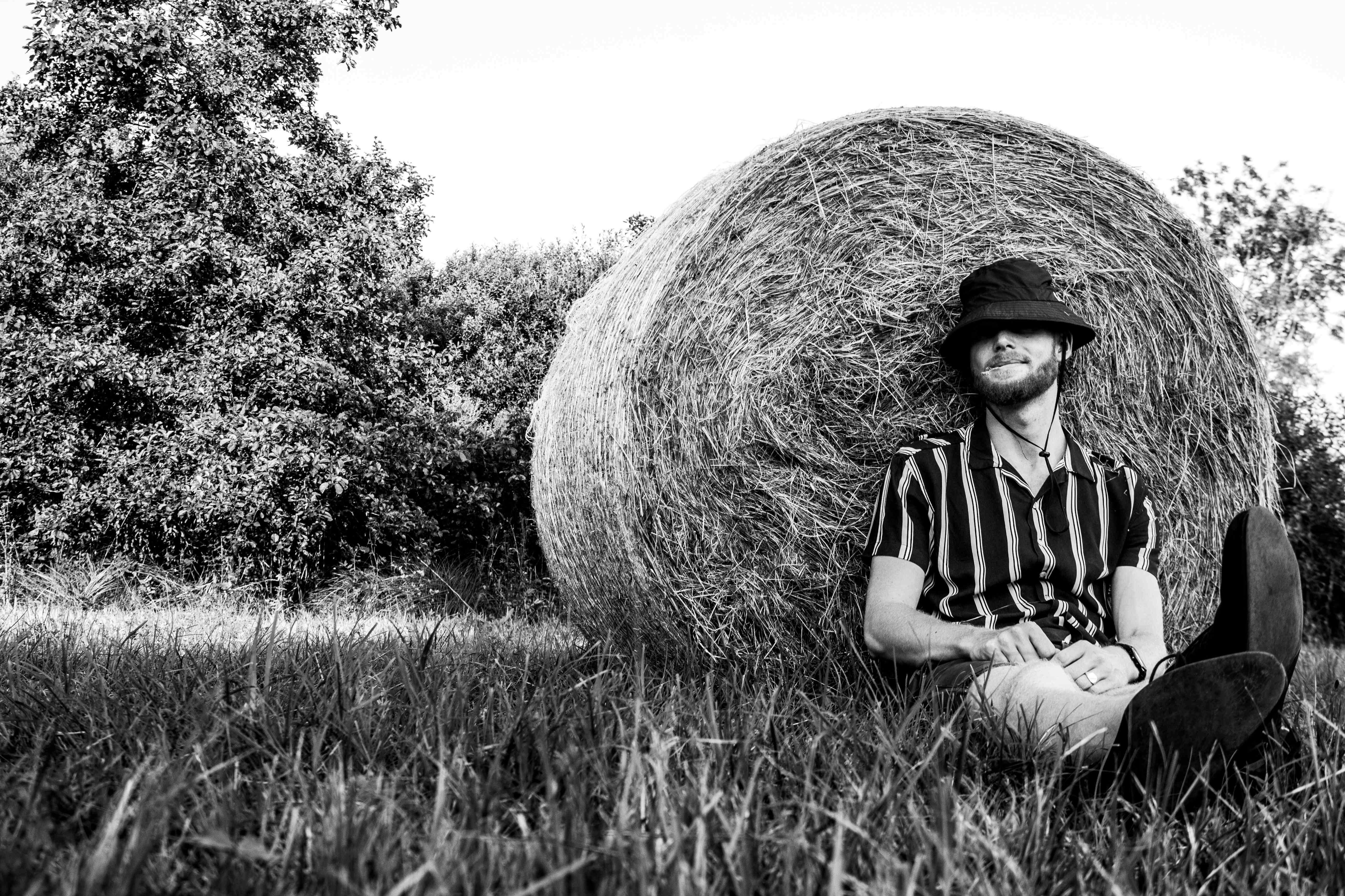 Jonge man met grasspriet in de mond tegen een hooibaal aan