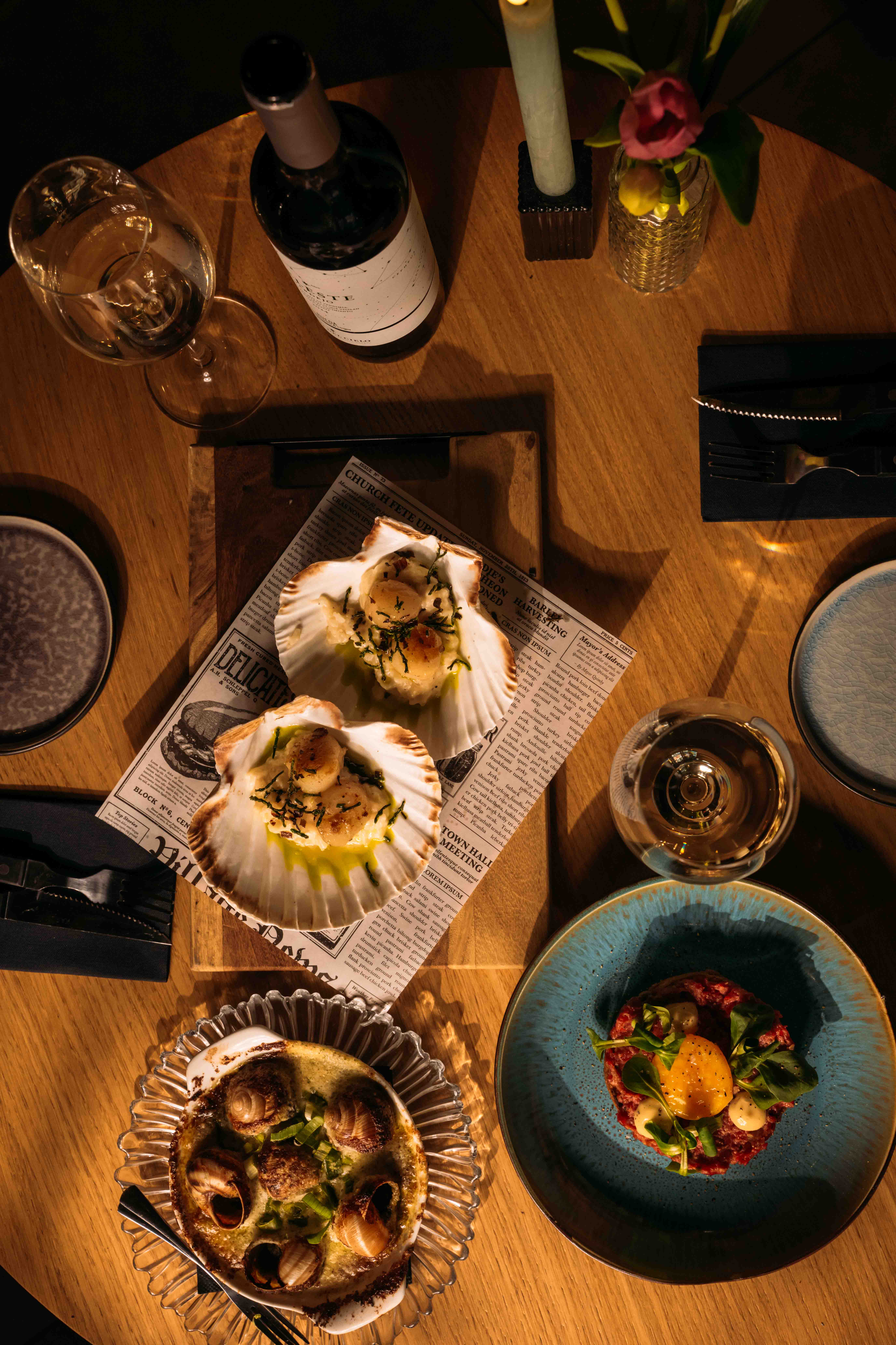 Bovenaanzicht van een houten tafel met coquilles in de schelp, escargots, tartaar, een fles wijn en een brandende kaars