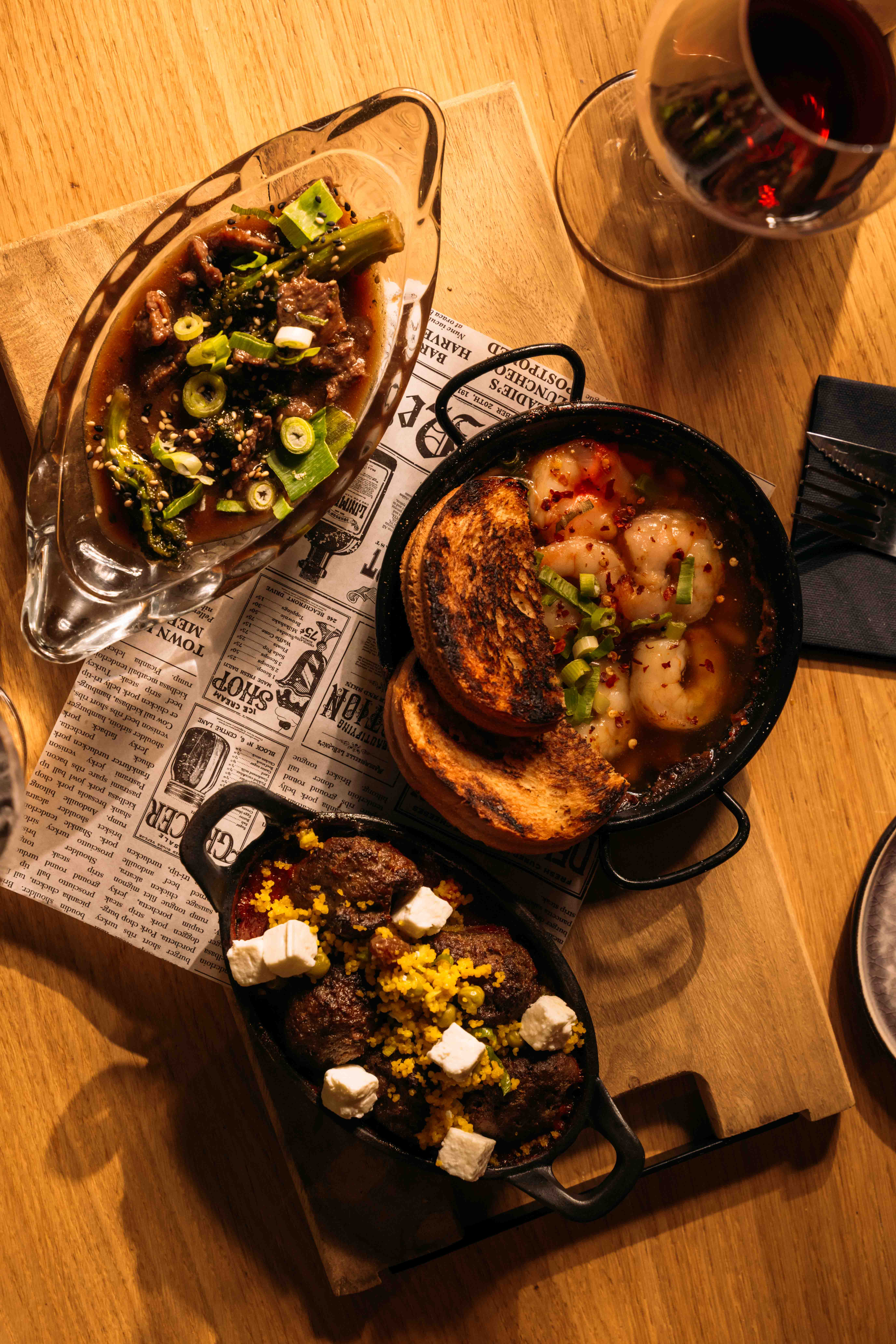Drie deelgerechtjes op een plank: Beef Bulgogi, Gamba's Pil Pil met geroosterd brood en gehaktballetjes met couscous en feta