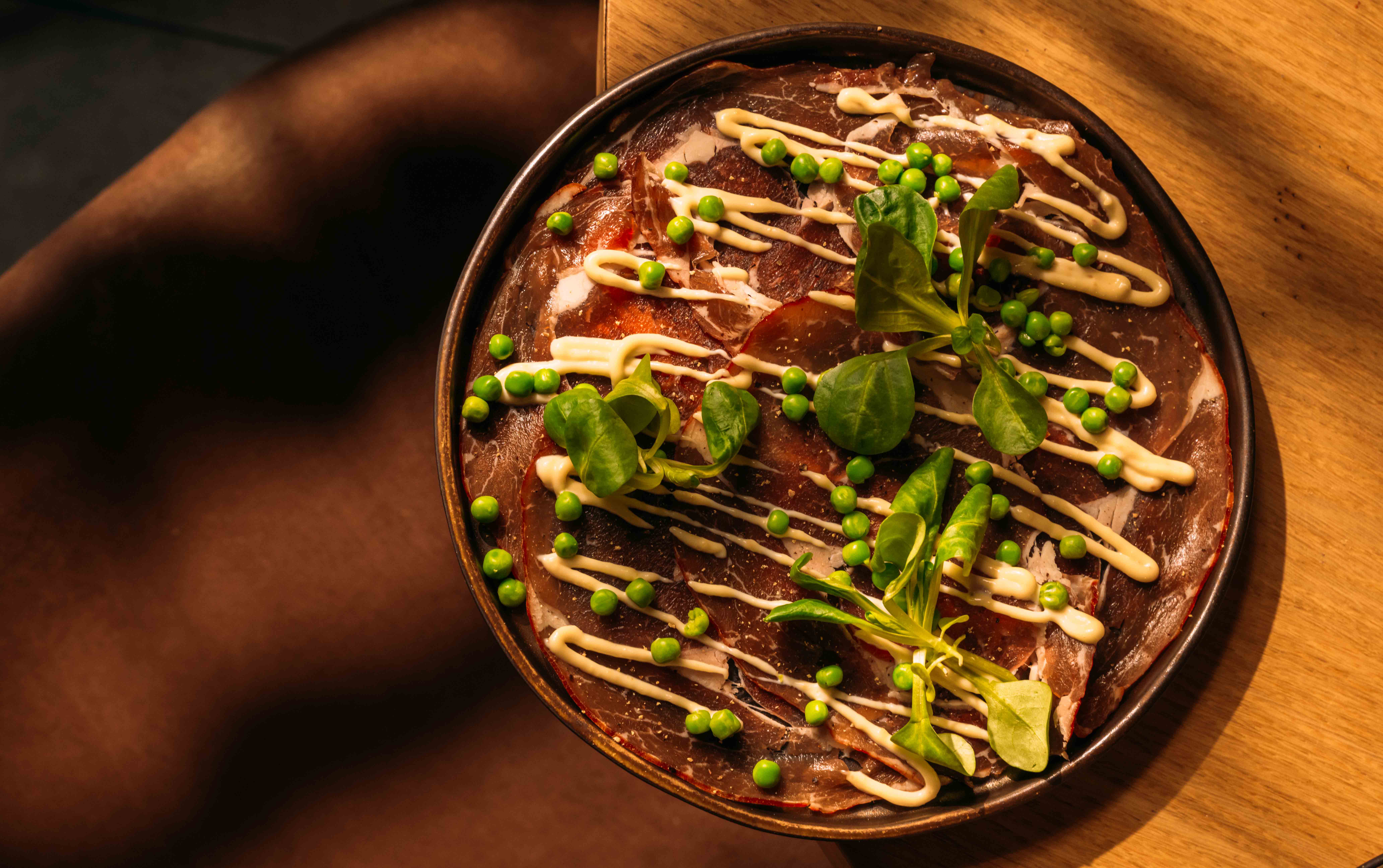 Schaal met dungesneden vlees, doperwten en cress op een houten plank in warm licht
