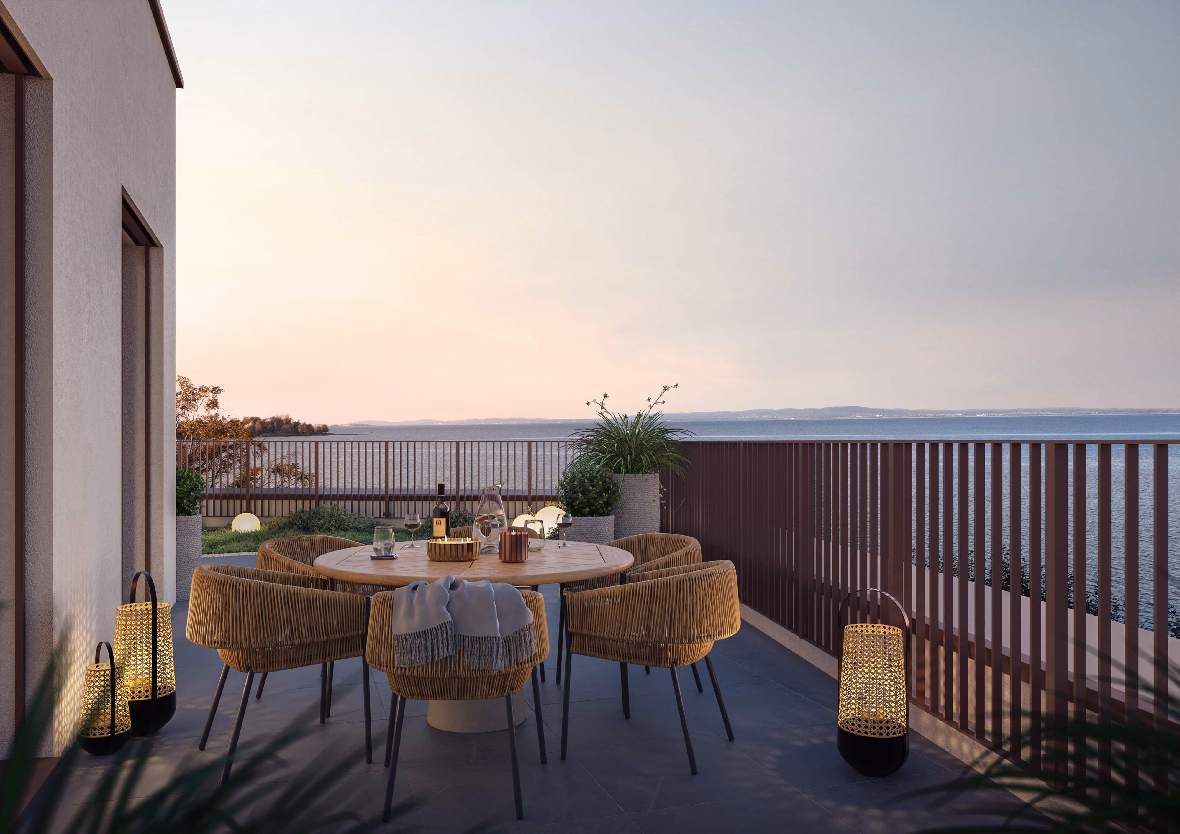 Terrasse mit einem runden Holztisch, Korbstühlen und Laternen mit Blick auf einen See bei Sonnenuntergang.