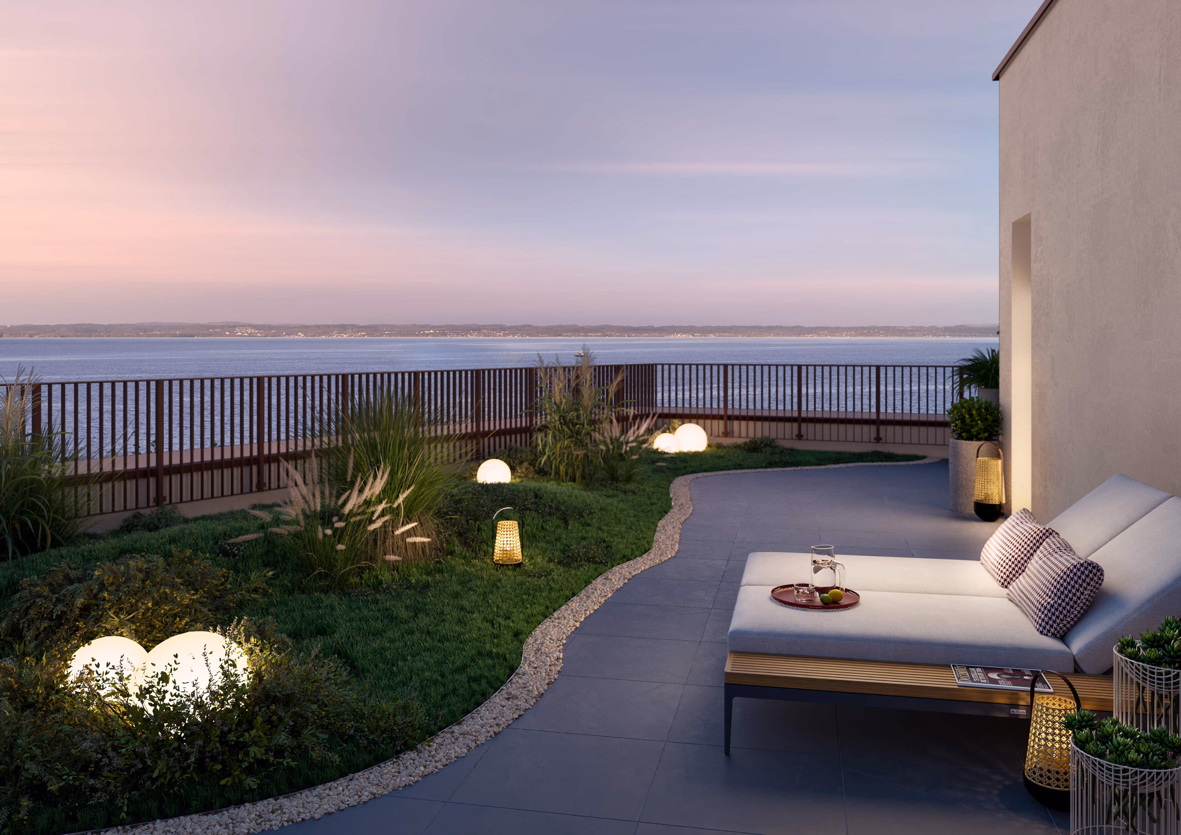 Terrassenbereich mit Liegestuhl, Pflanzen und Lichtern mit Blick auf ruhigen See bei Sonnenuntergang.
