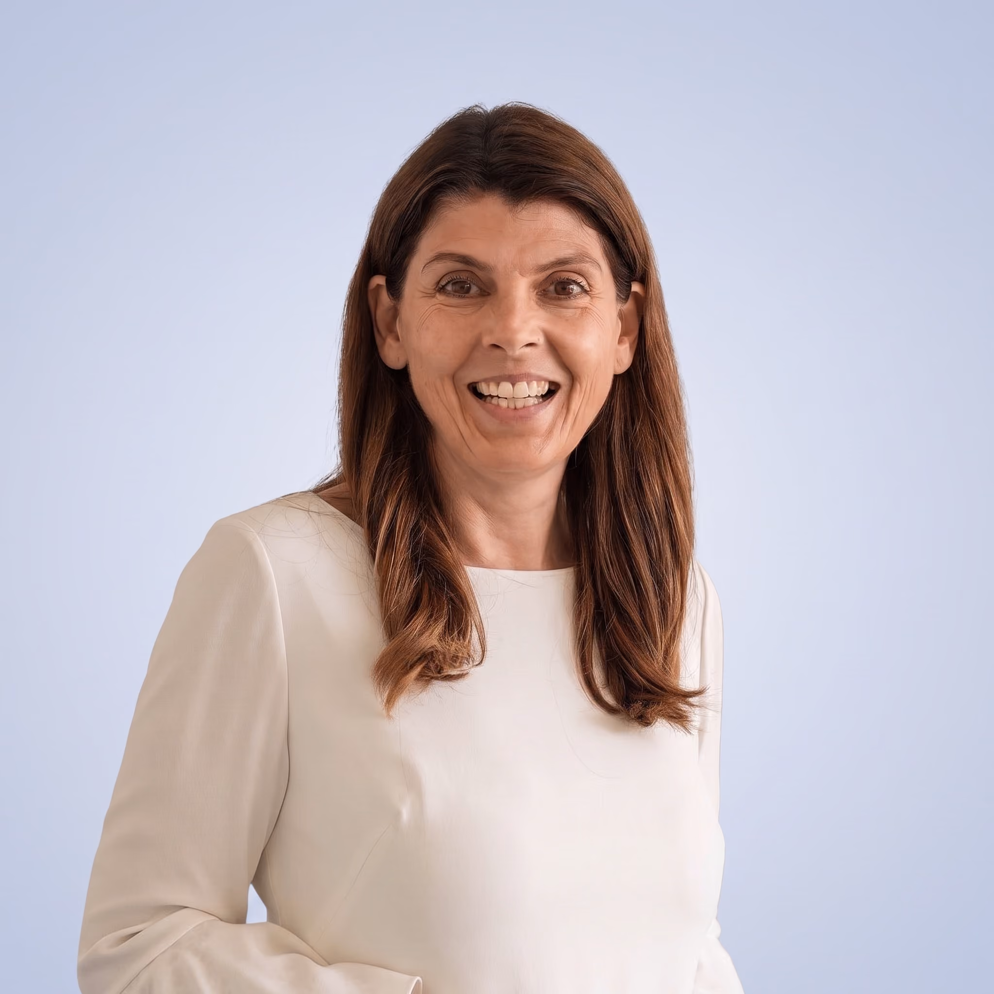Fröhliche Frau mit langen braunen Haaren und hellem Oberteil vor hellem Hintergrund.