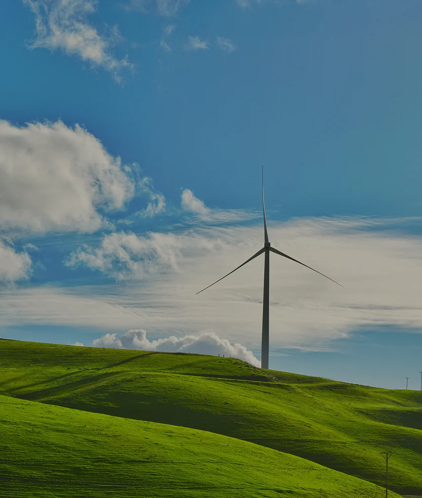 Single wind turbine on green rolling hills under a partly cloudy blue sky.