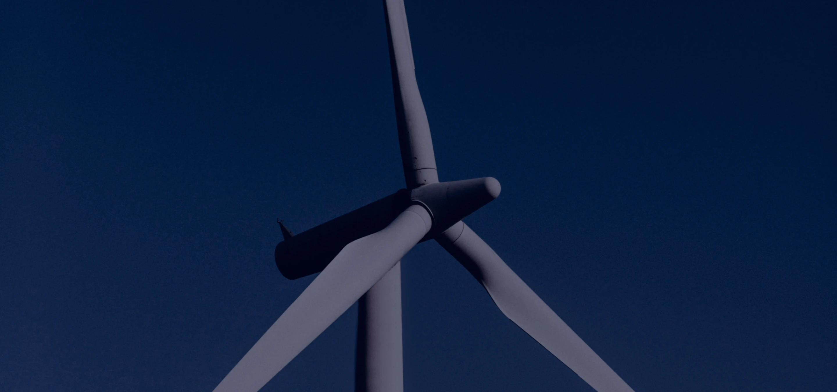 Close-up of a white wind turbine with three blades against a clear dark blue sky.