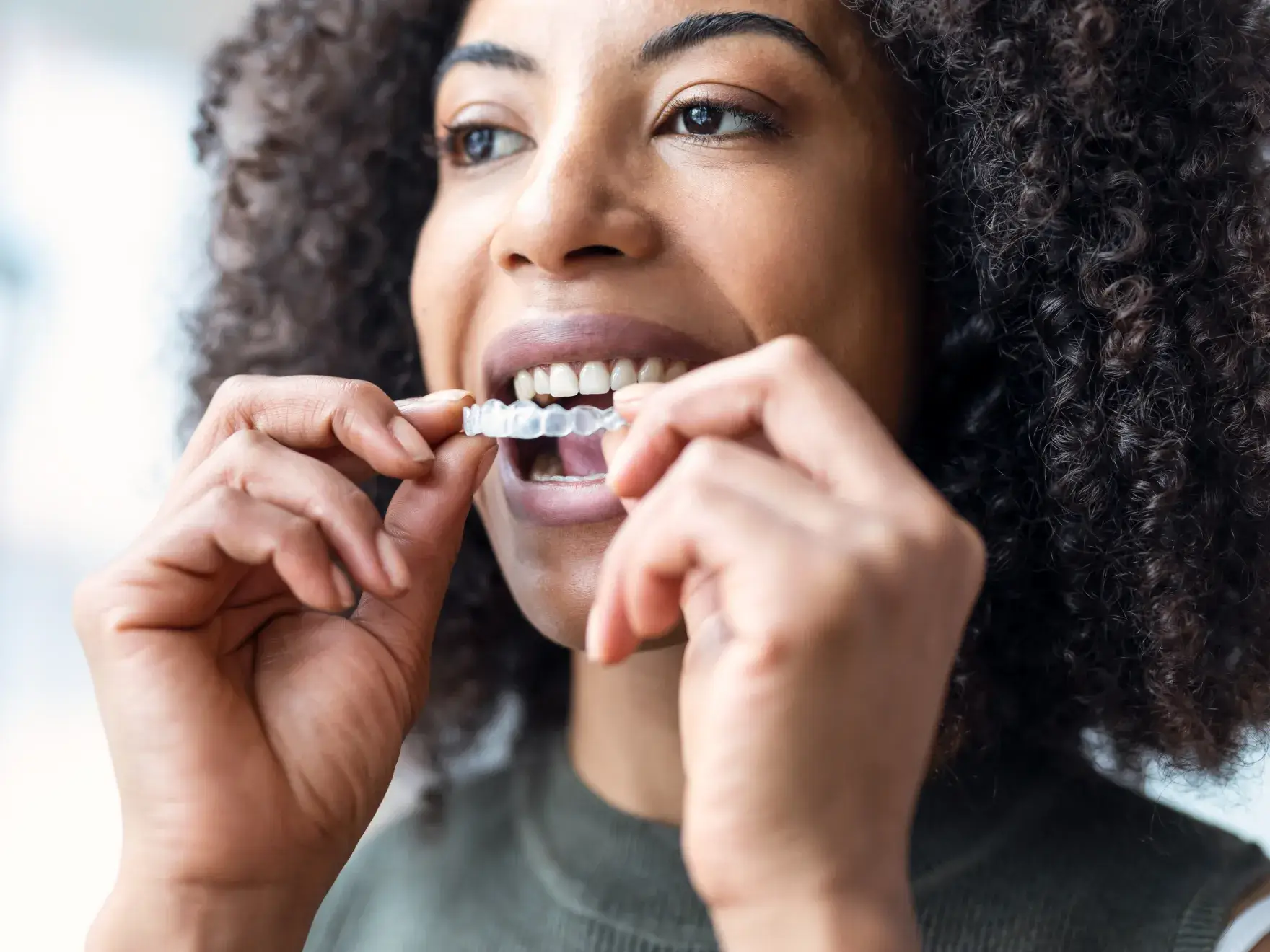 A photo of a person placing a clear dental aligner on their teeth.
