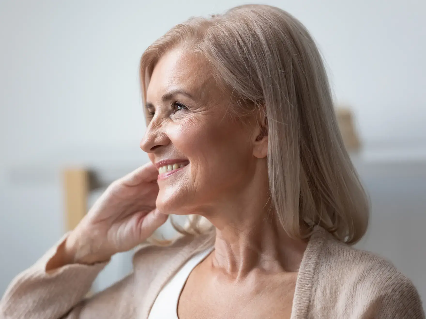 A photo of a smiling older woman with long, light hair, looking to the left, wearing a light sweater.