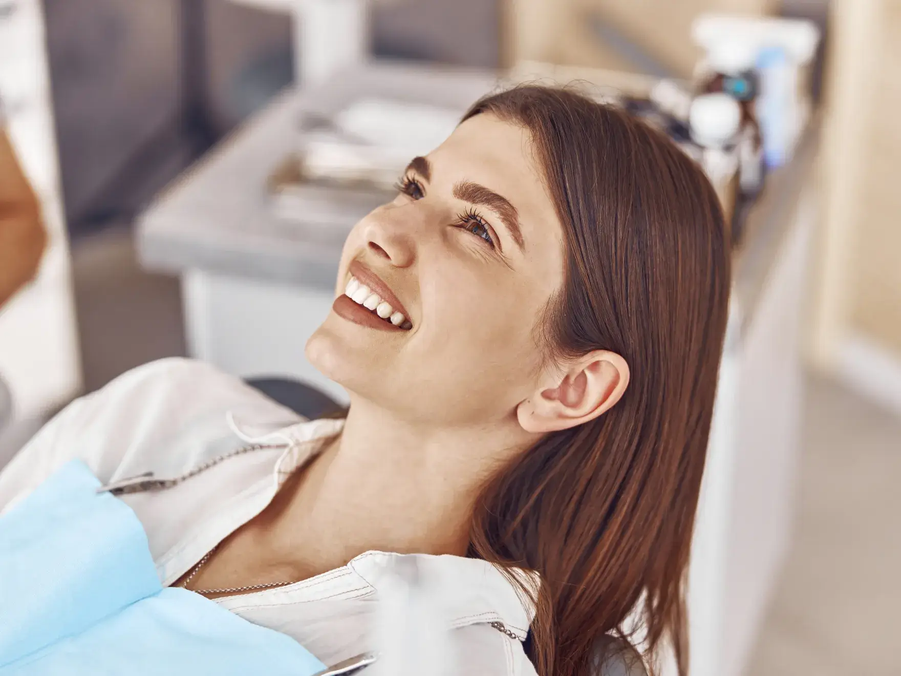 A photo of a woman with brown hair smiling while sitting in a dental chair.
