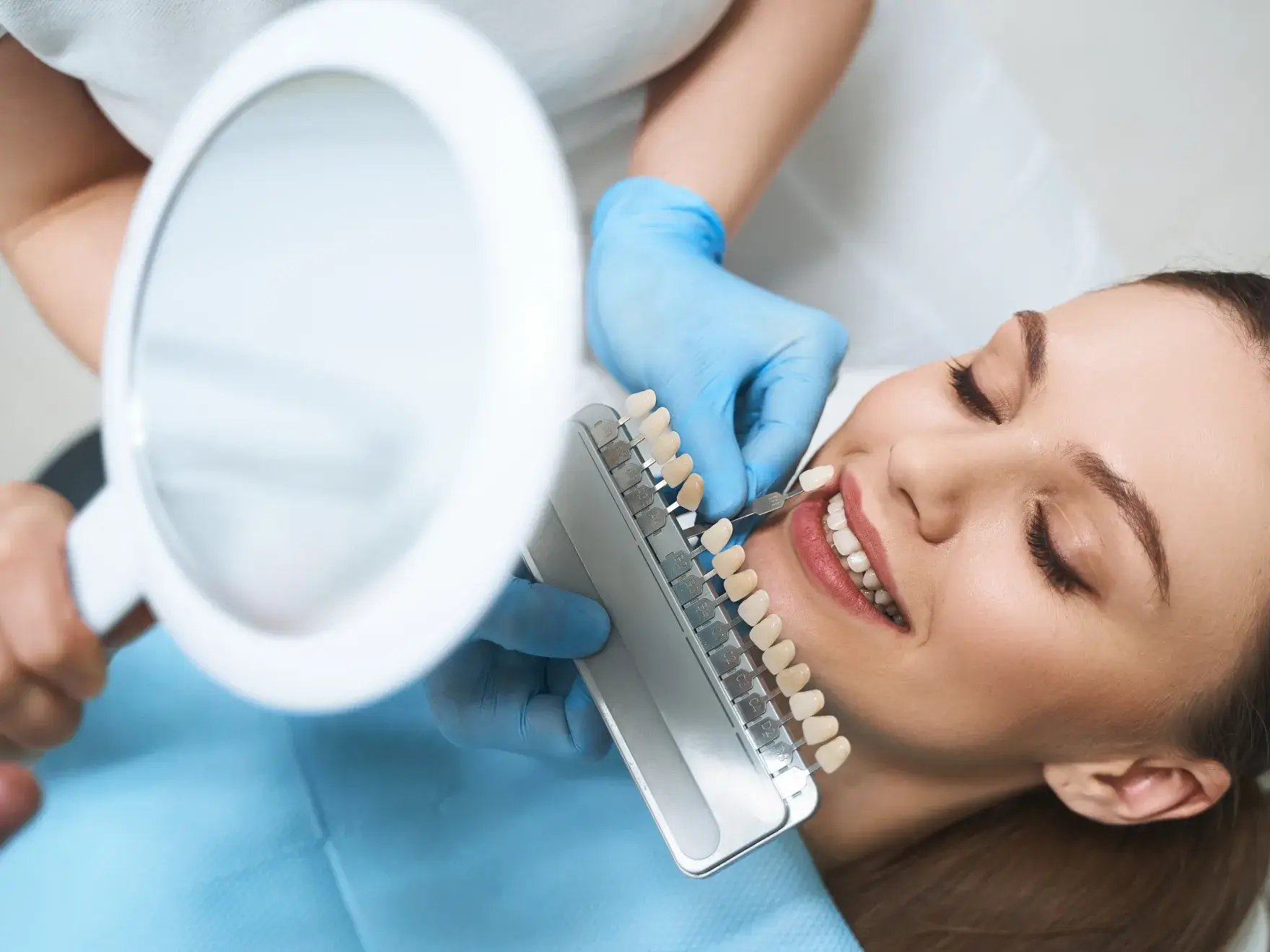 A dentist compares a shade guide to a smiling patient's teeth.