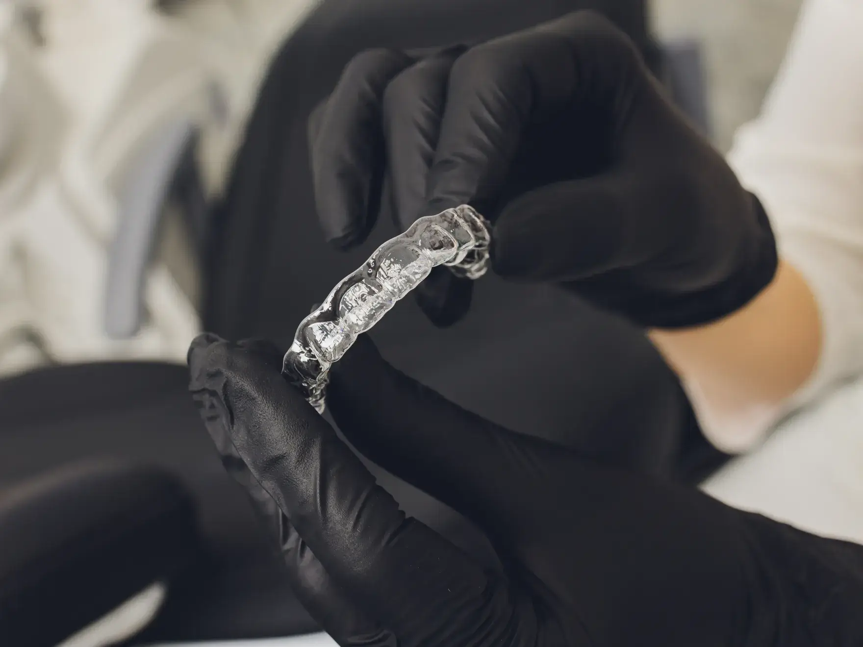 A person wearing black gloves holds a clear dental aligner.