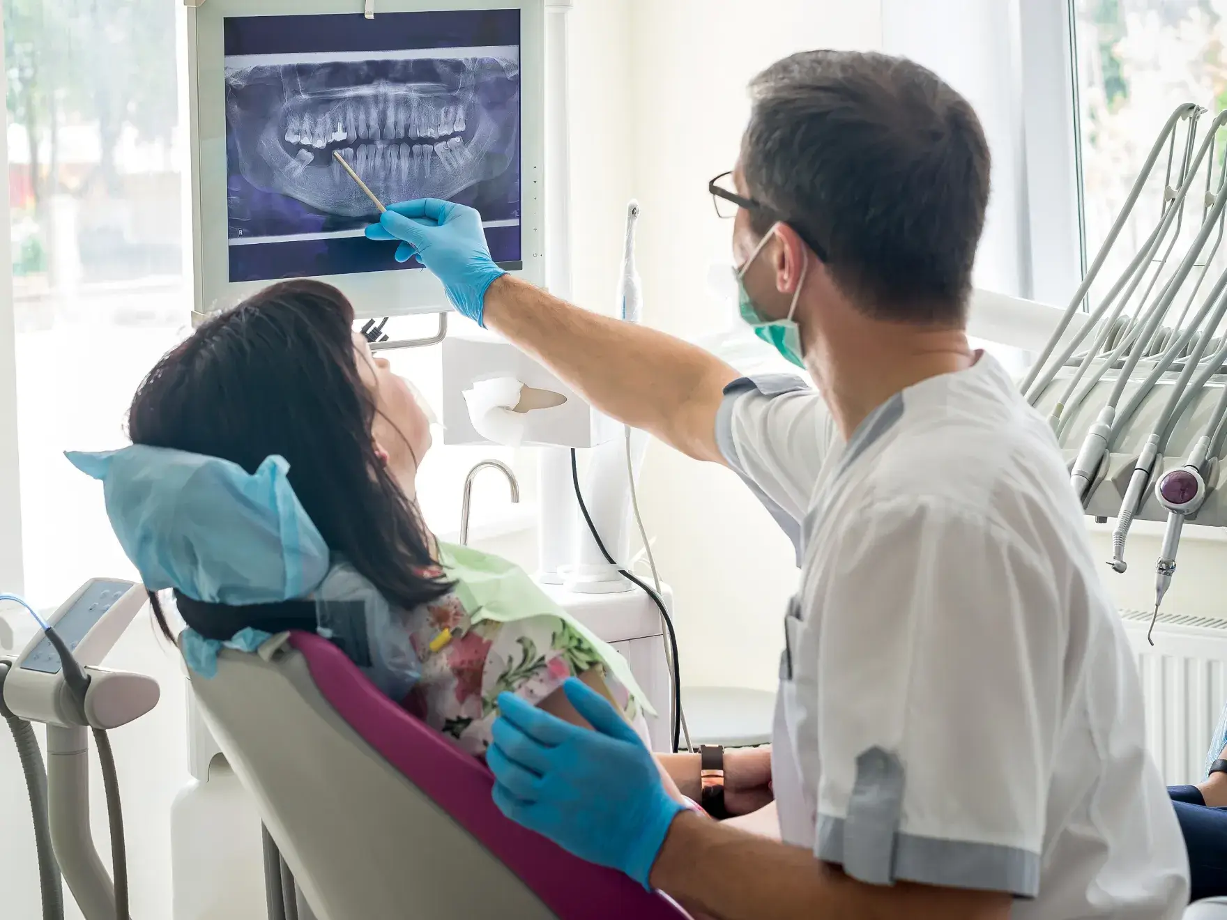 A dentist shows a seated patient their dental X-ray on a screen.