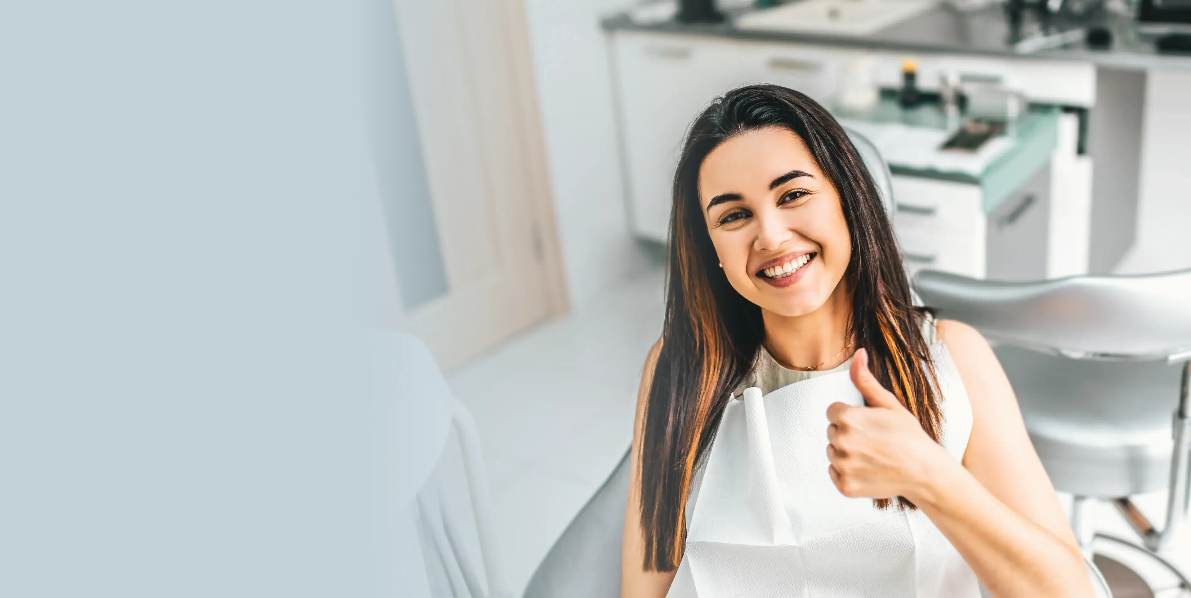 A photo of a woman in a dental office smiling and giving a thumbs-up.