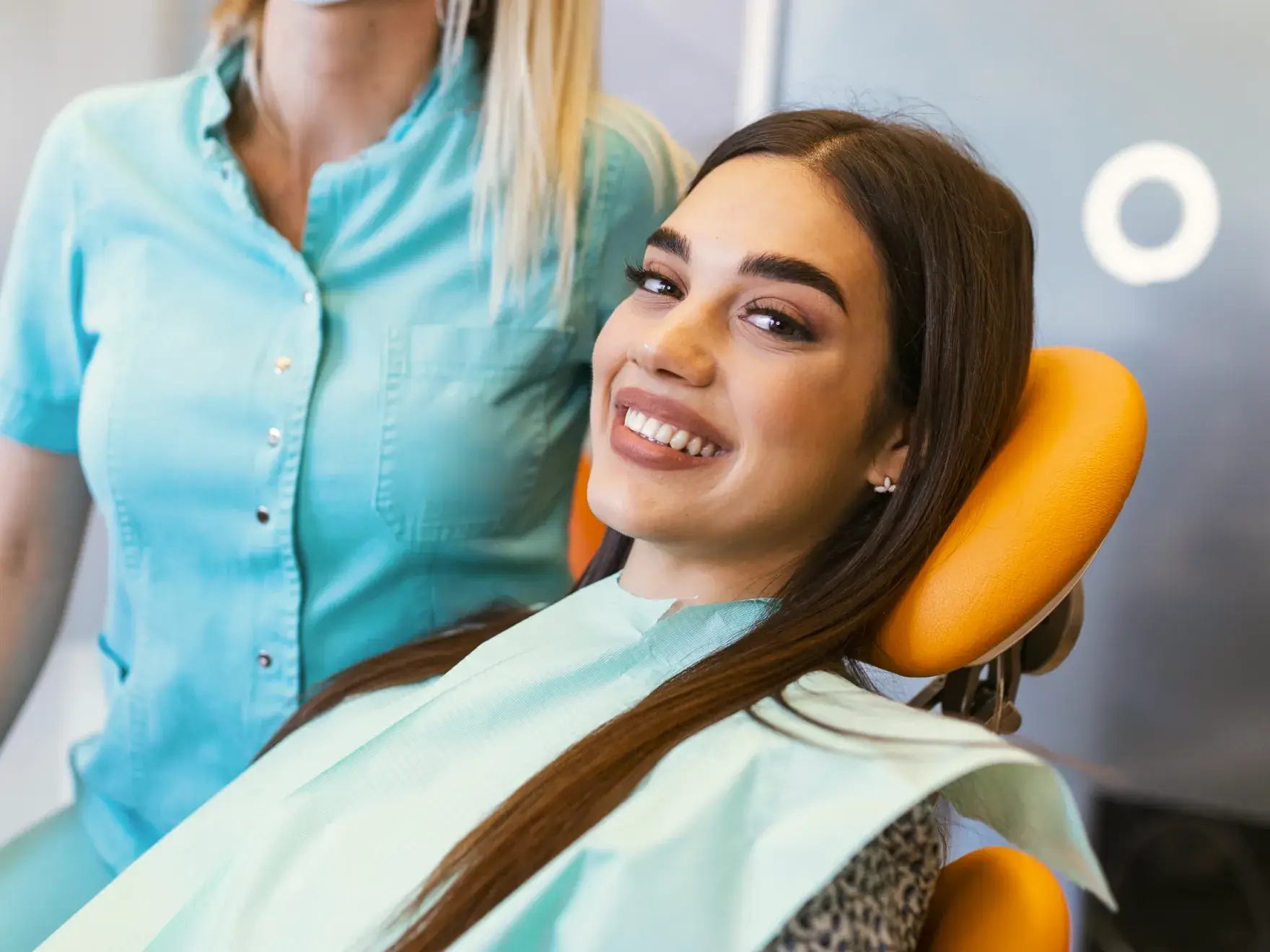 A photo of a woman smiling in a dental chair with a dentist nearby.