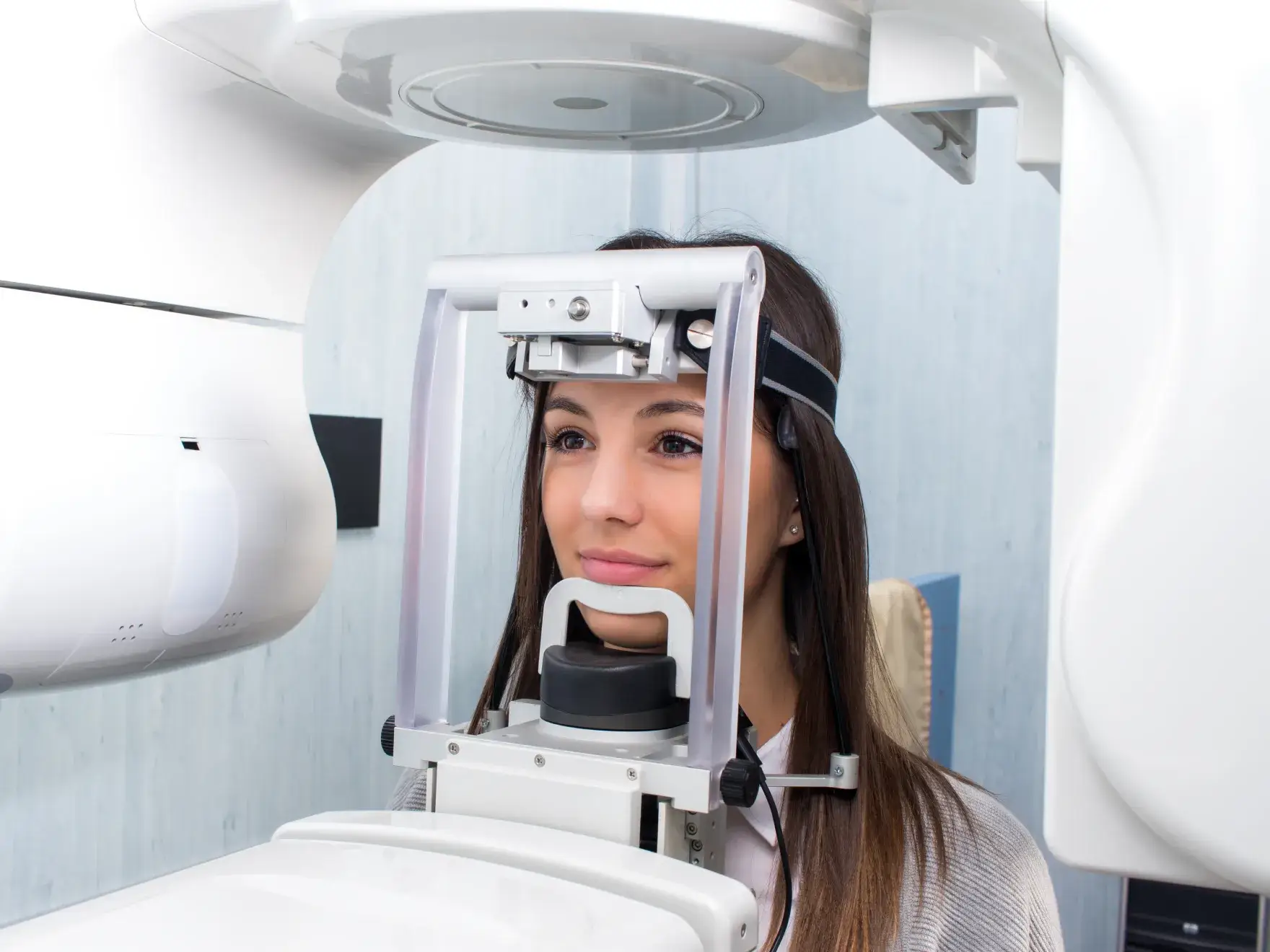 A photo of a woman with long hair getting a dental x-ray. She's sitting with her head in a white machine.