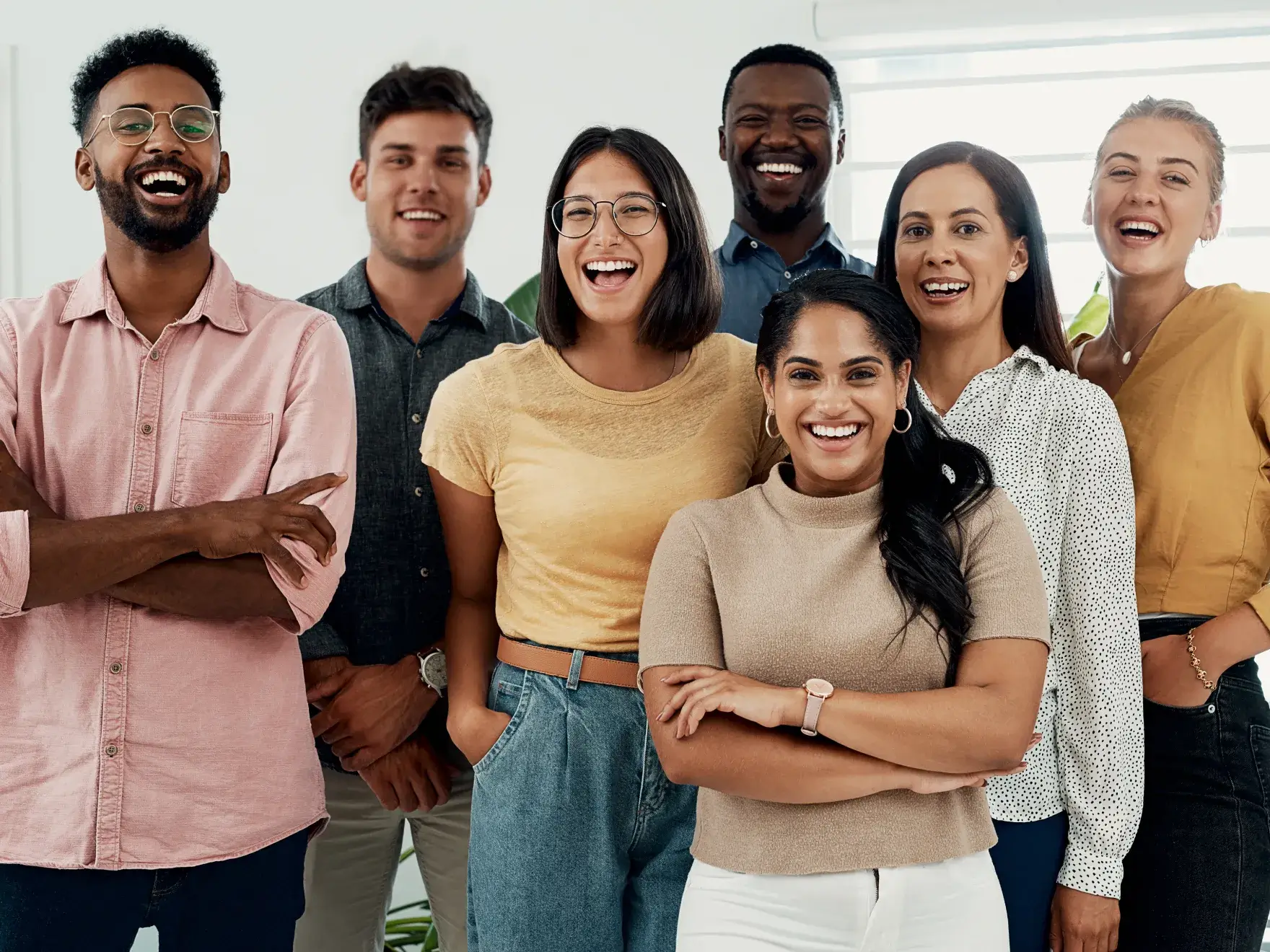 A photo of seven diverse people standing and smiling in a bright room.