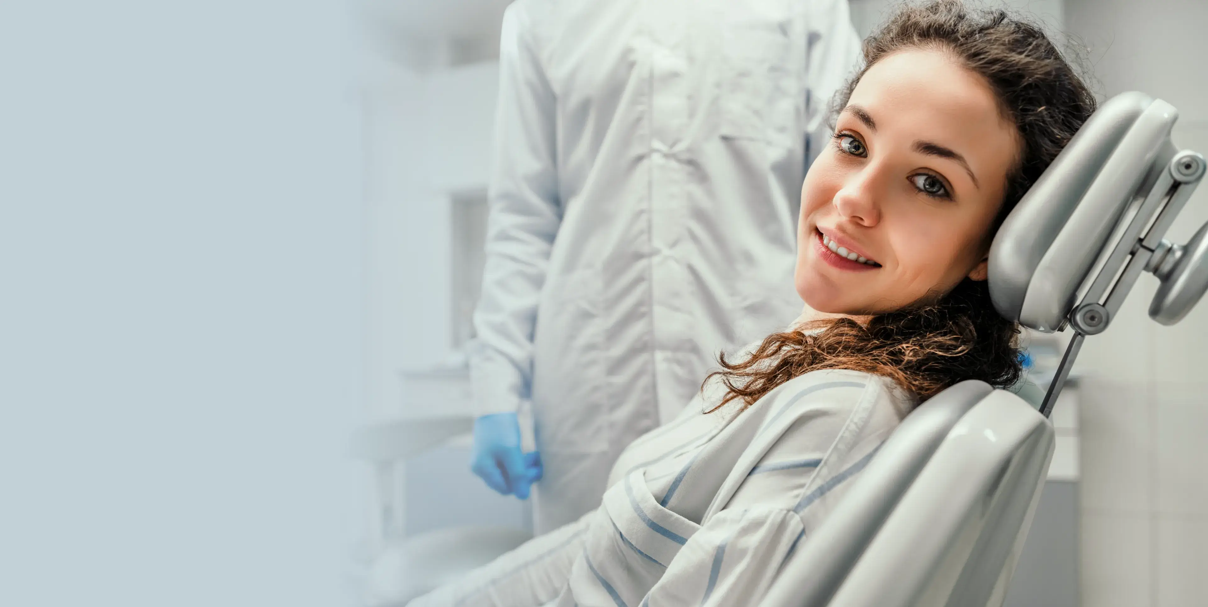 A woman smiling in a dental chair with a dentist beside her in the office.