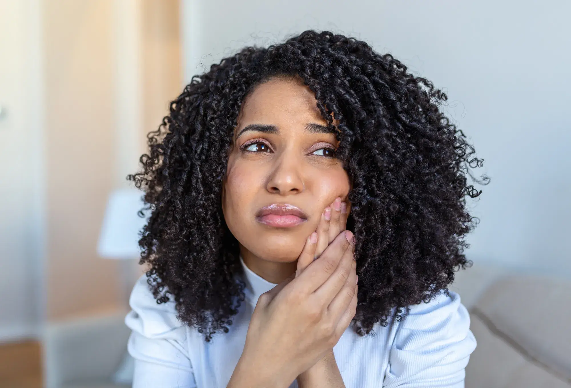 A photo of a woman with curly hair holding her cheek, looking worried.
