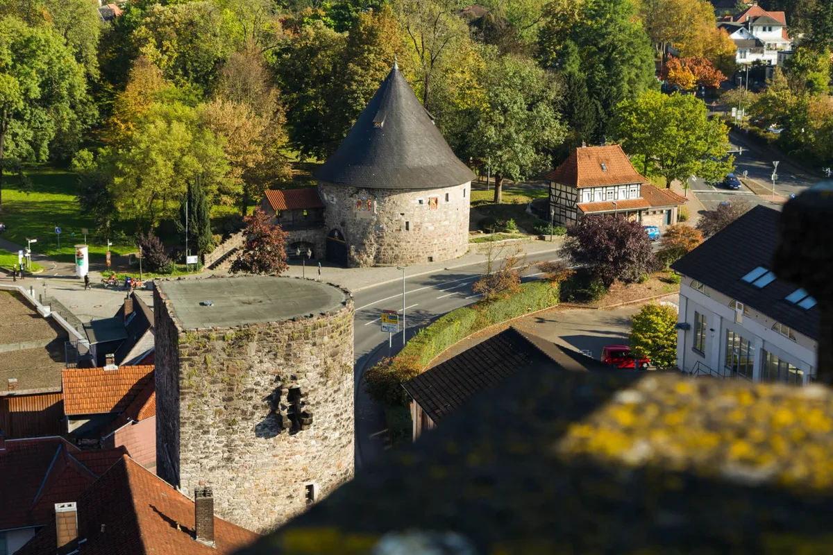 Blick über die Altstadt von Hann. Münden auf einen runden Wehrturm mit spitzem Schieferdach, davor ein zweiter Turmstumpf, daneben ein Fachwerkhaus und herbstlich gefärbte Bäume.
