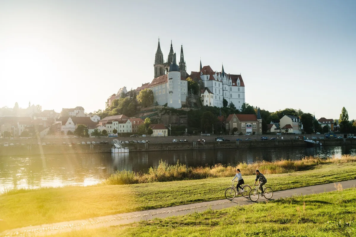 Zwei Radfahrende auf dem Elbuferweg, gegenüber erheben sich Albrechtsburg und Meißner Dom über der Altstadt