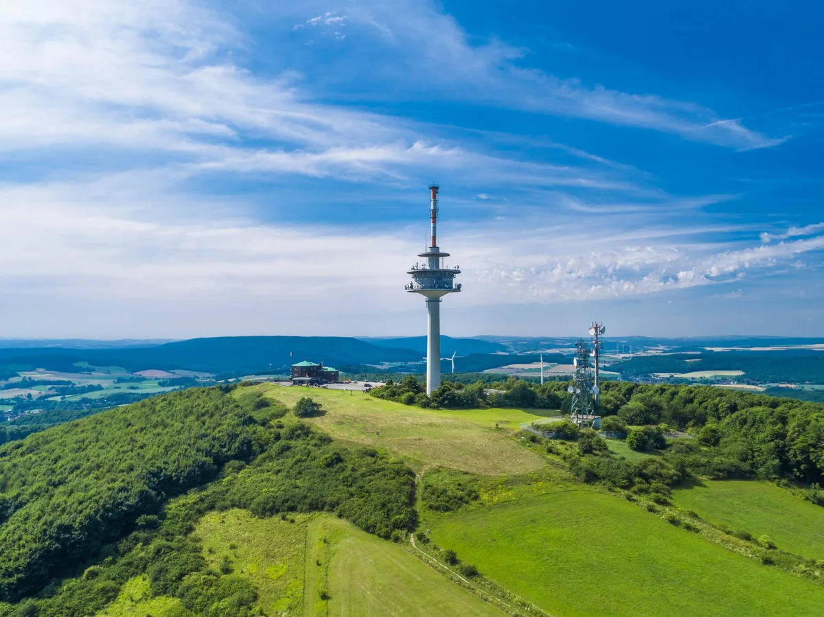 Die bewaldete Kuppe des Köterbergs mit dem Sendeturm, ringsum Wiesen und die Hügel des Weserberglands