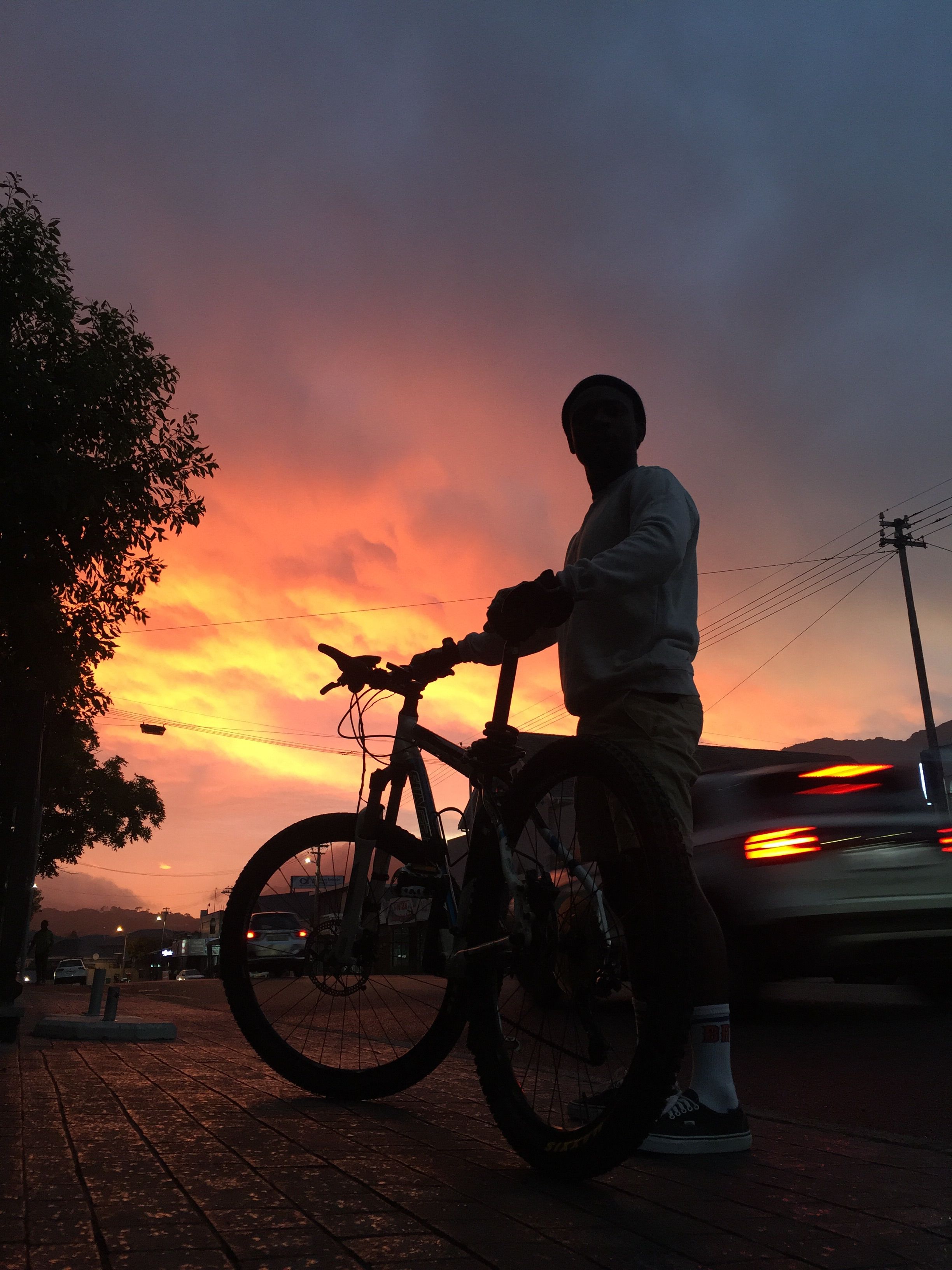 Silhouette eines Radfahrers vor dämmrigem Abendhimmel über einer Stadt, Straßenlaternen und Gebäudeumrisse im Hintergrund