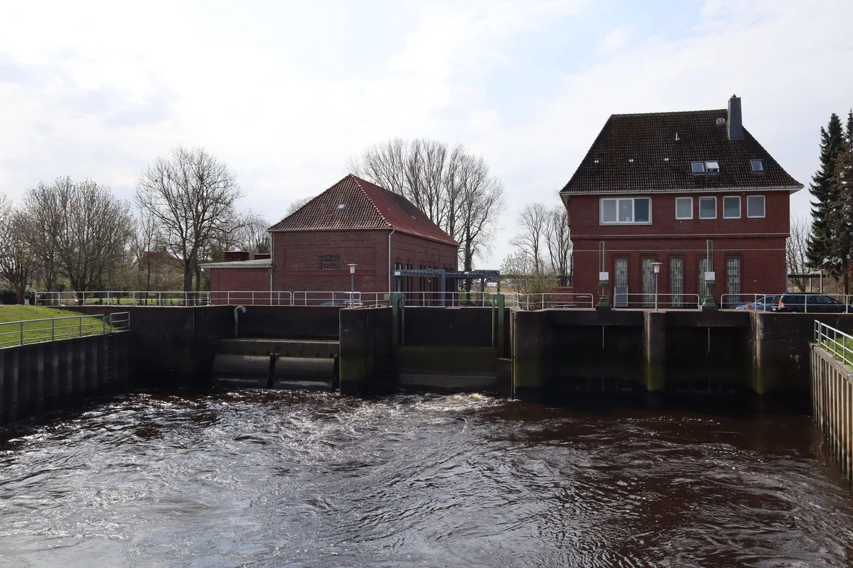 Zwei rote Backsteingebäude an einem Auslaufbauwerk, davor aufgewühltes Wasser zwischen Betonwänden