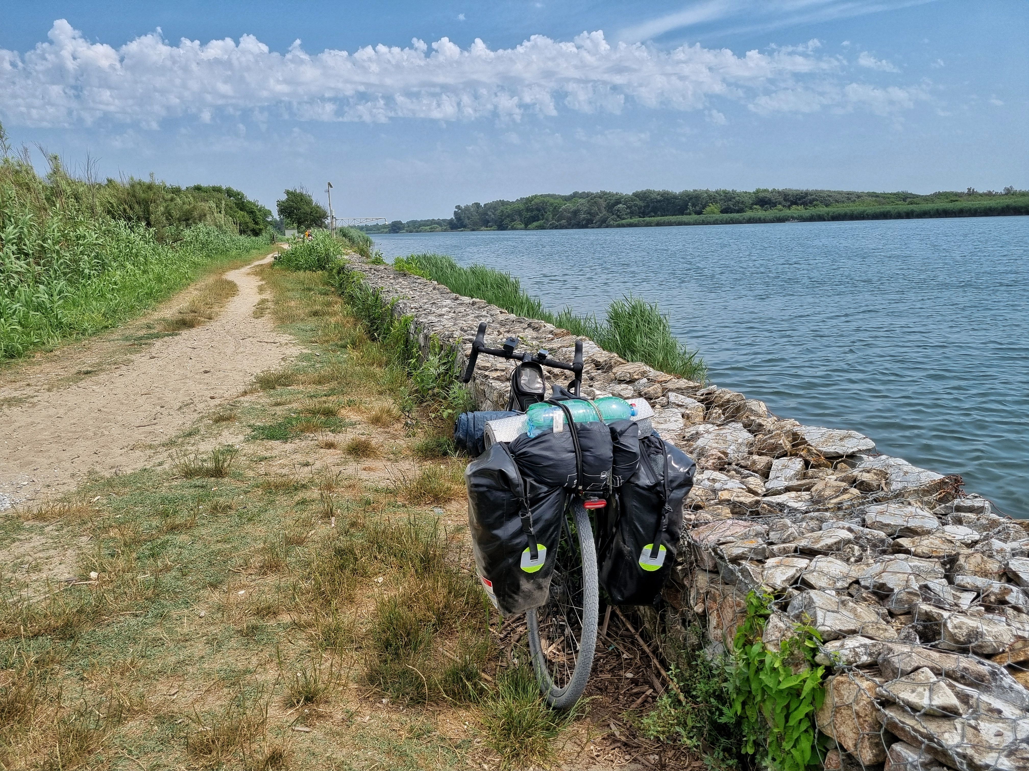 Bepacktes Reiserad steht an einer Bruchsteinmauer am Wasser, daneben ein unbefestigter Uferweg