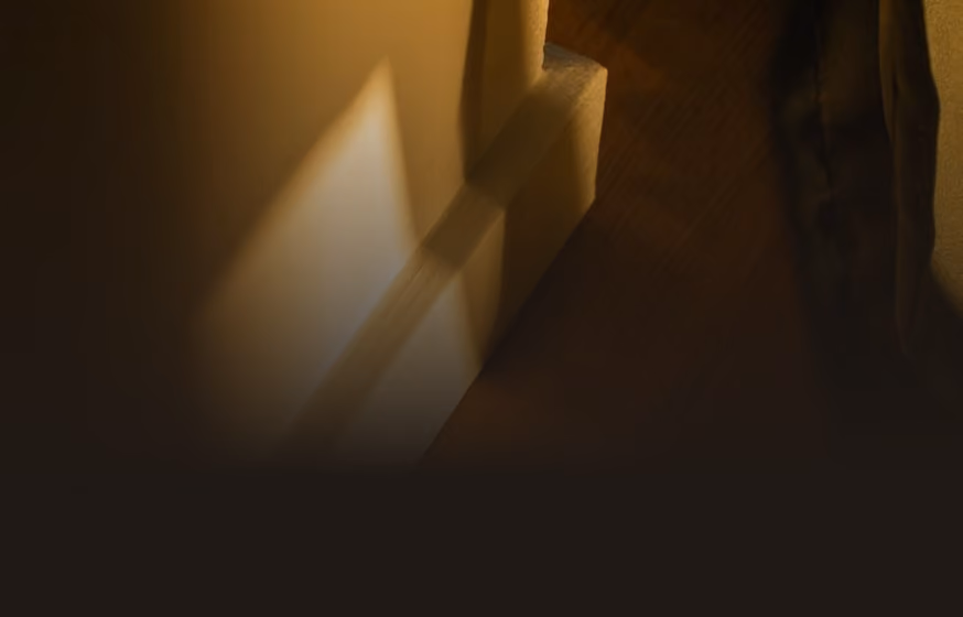 Dimly lit narrow corridor with faint illuminating light casting shadows on the wall, creating a warm, muted atmosphere.