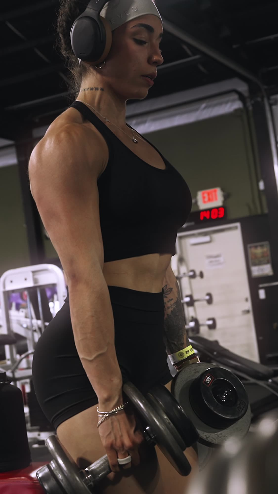 Roxy mid-set with dumbbells, headphones on, shot from the side