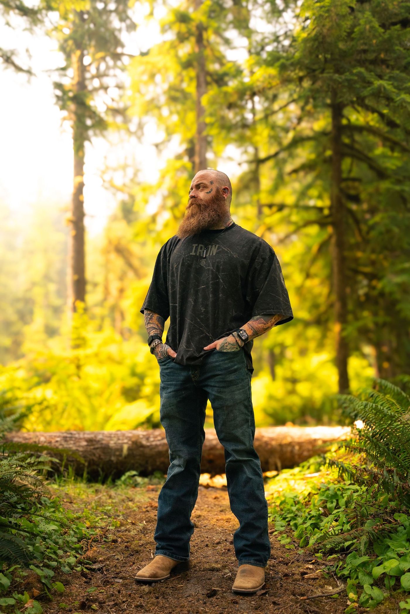Standing in a sunlit forest in an Iron Sanctuary tee, hands in pockets, looking off frame