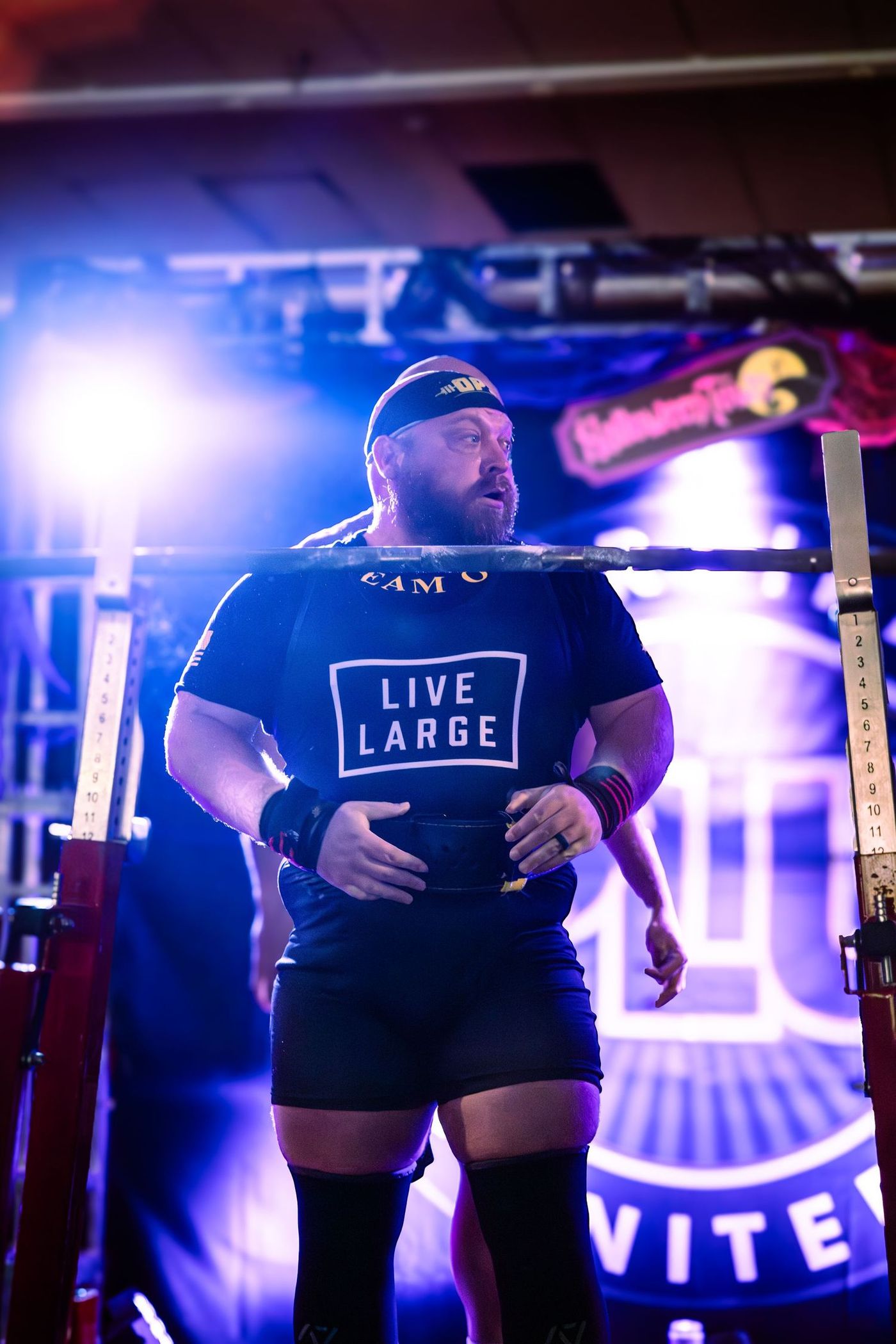 Lifter in a Live Large tee standing on the platform between attempts