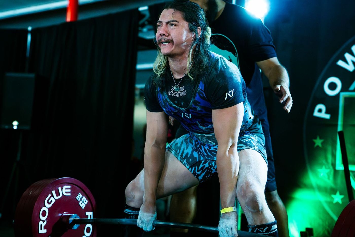 Lifter grimacing through a deadlift, Powerlifting United logo lit green behind him