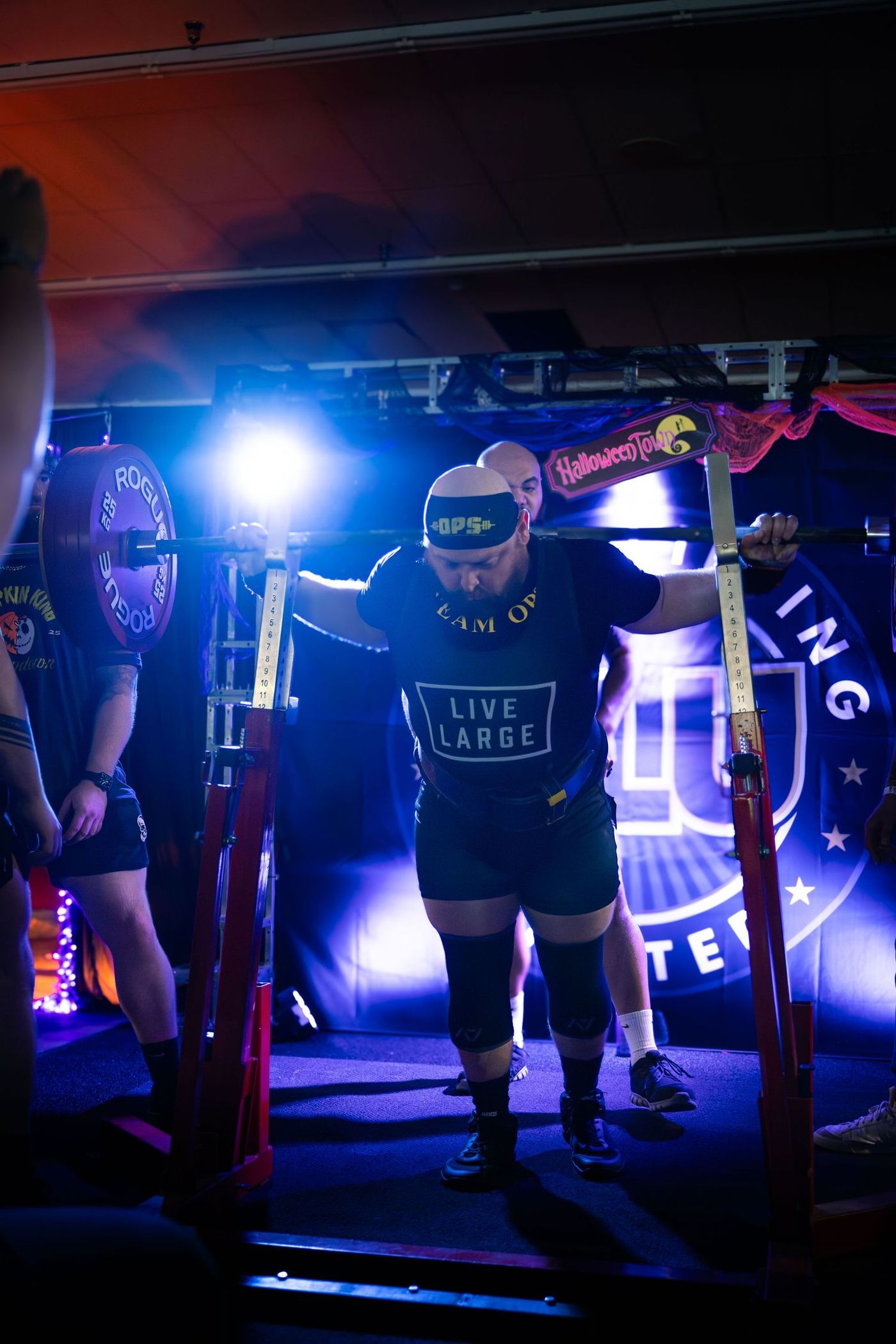 Lifter walking out to the rack under blue stage light at a Powerlifting United meet