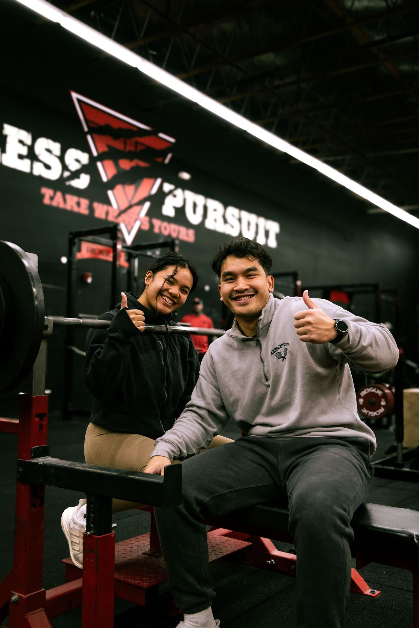 Two Training Grounds members on a bench giving a thumbs up, gym wall mural behind them