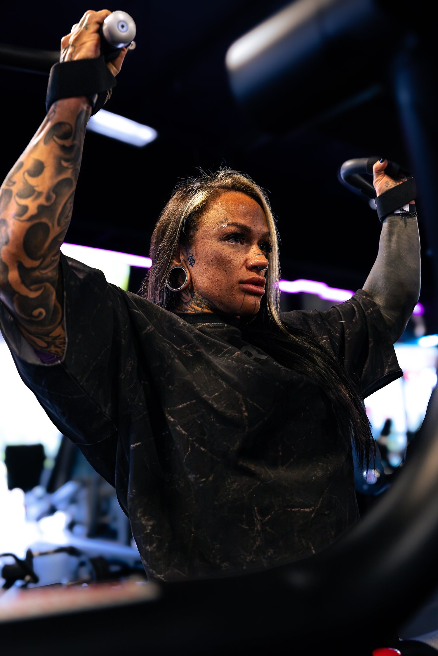 Jordain Sue pulling a rope overhead on the cable stack, sleeve tattoo in frame