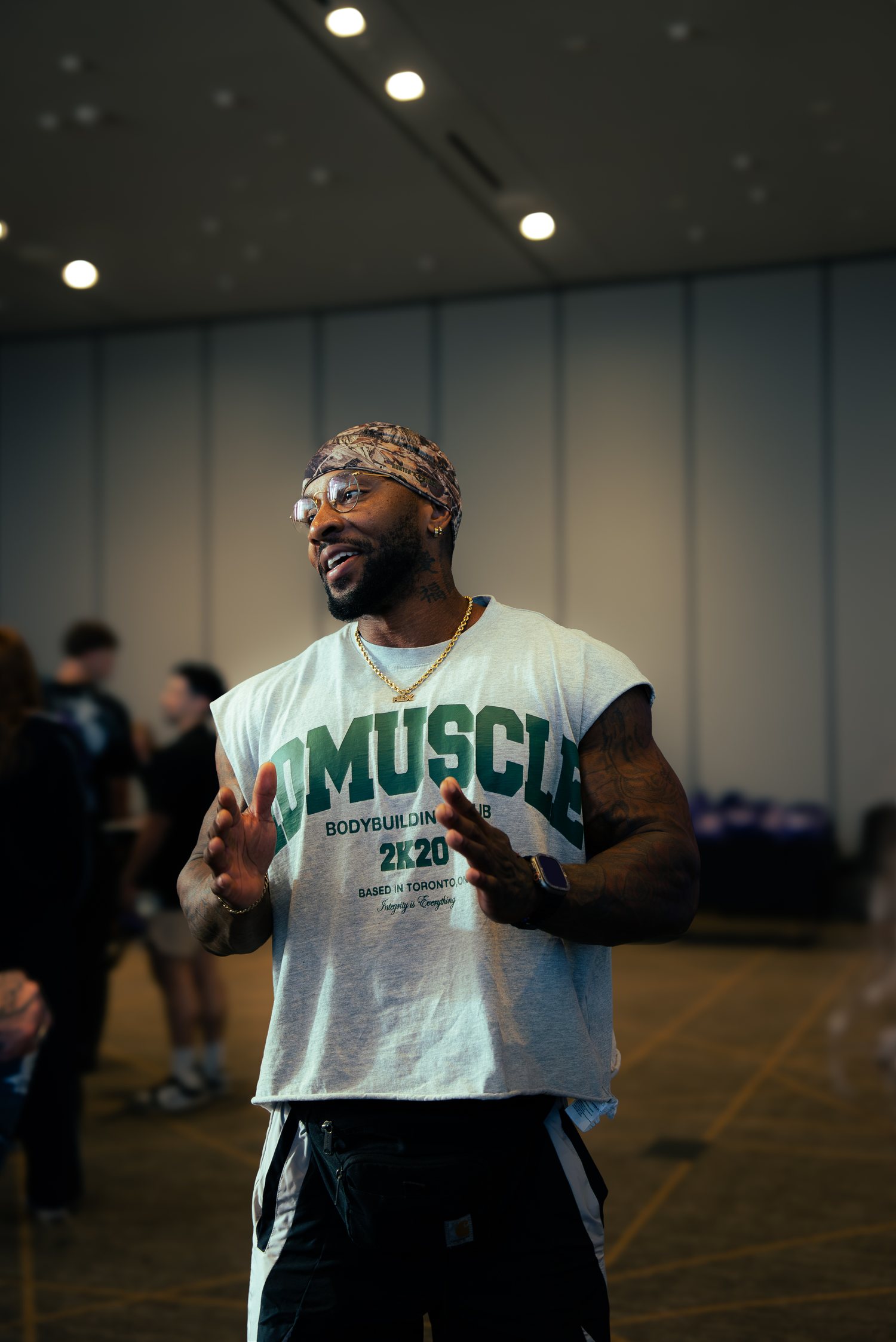 RIKFLEX in a bandana, glasses and a bodybuilding club tee, mid-conversation in a convention hall