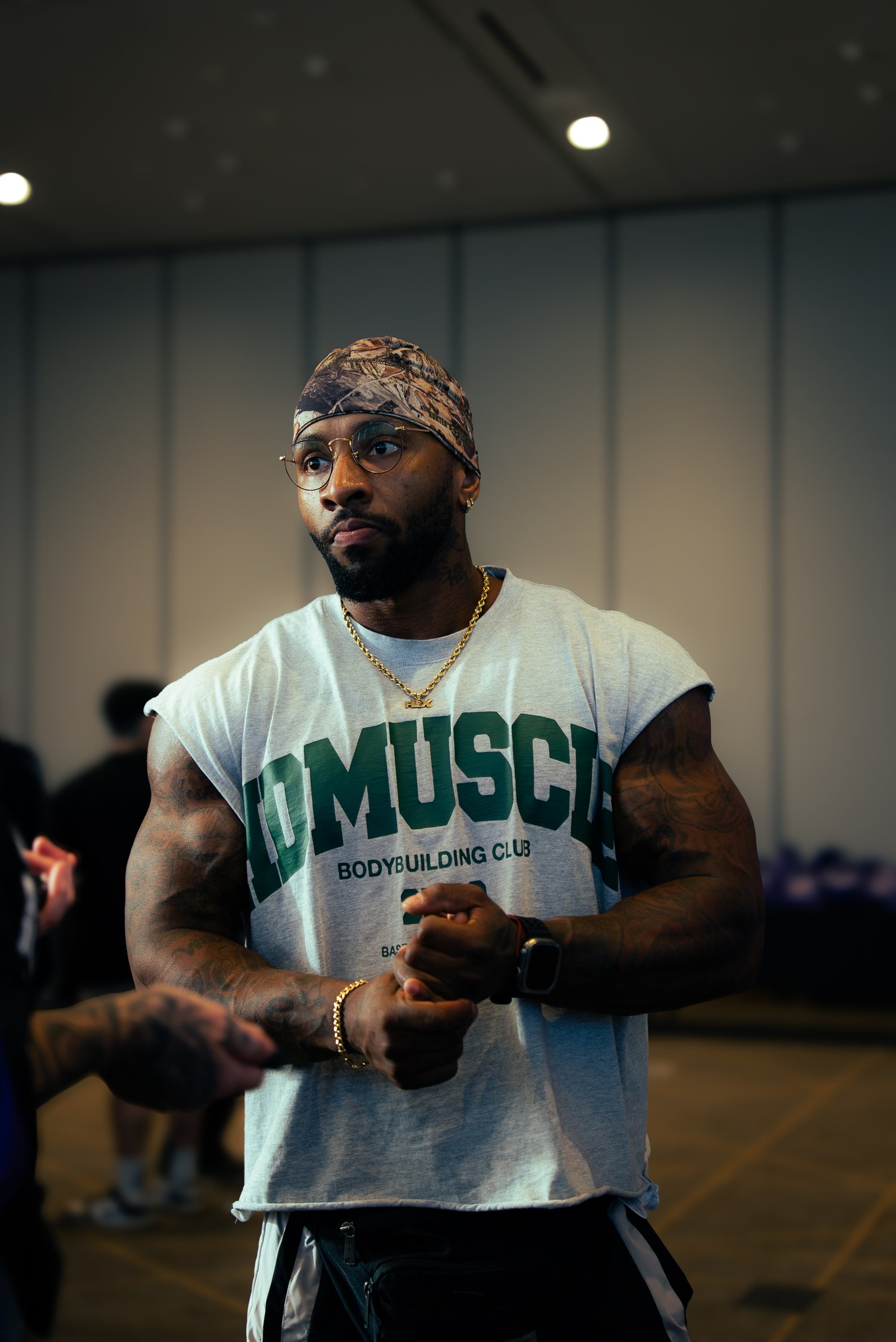 RIKFLEX in a bandana and gold chain, hands clasped, in a convention hall